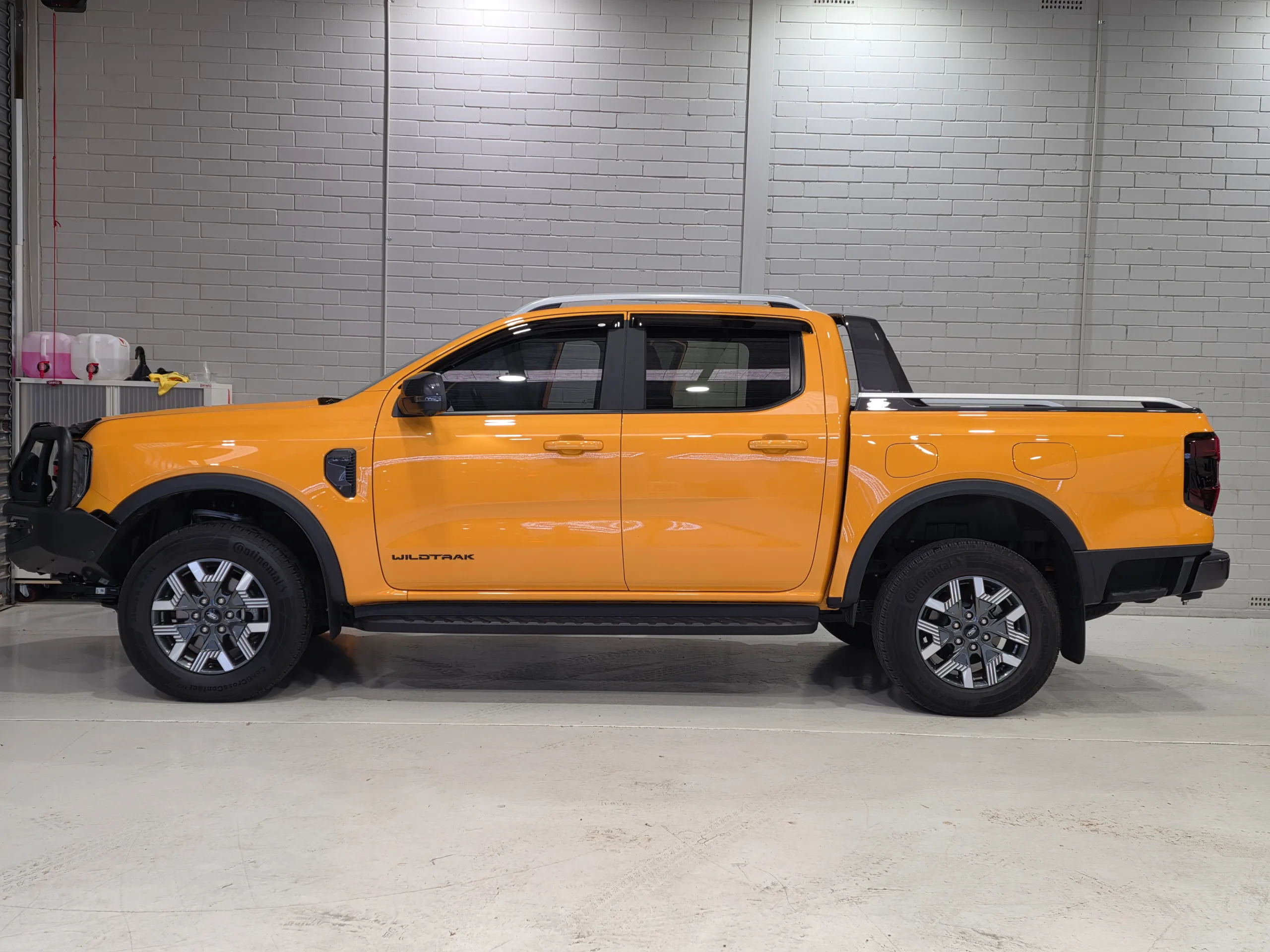 Gloss orange Ford Ranger Wildtrak PHEV in side profile, with a bull bar and sports bar