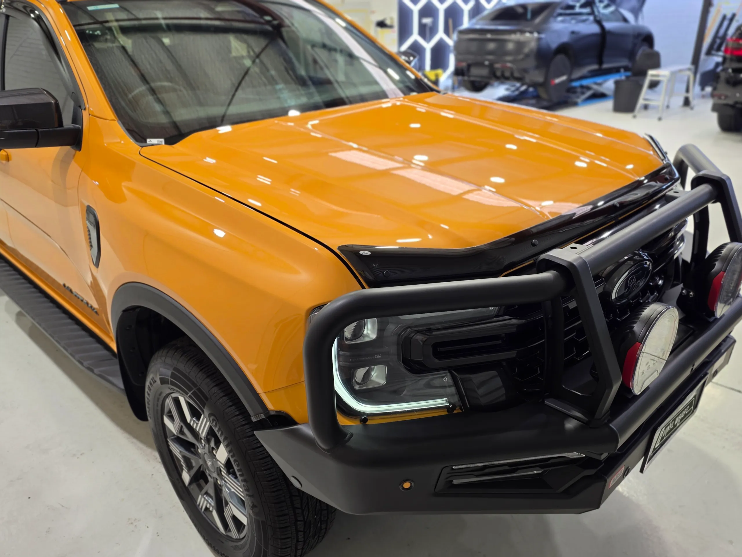 Orange Ford Ranger Wildtrak PHEV front quarter and bull bar under workshop lights