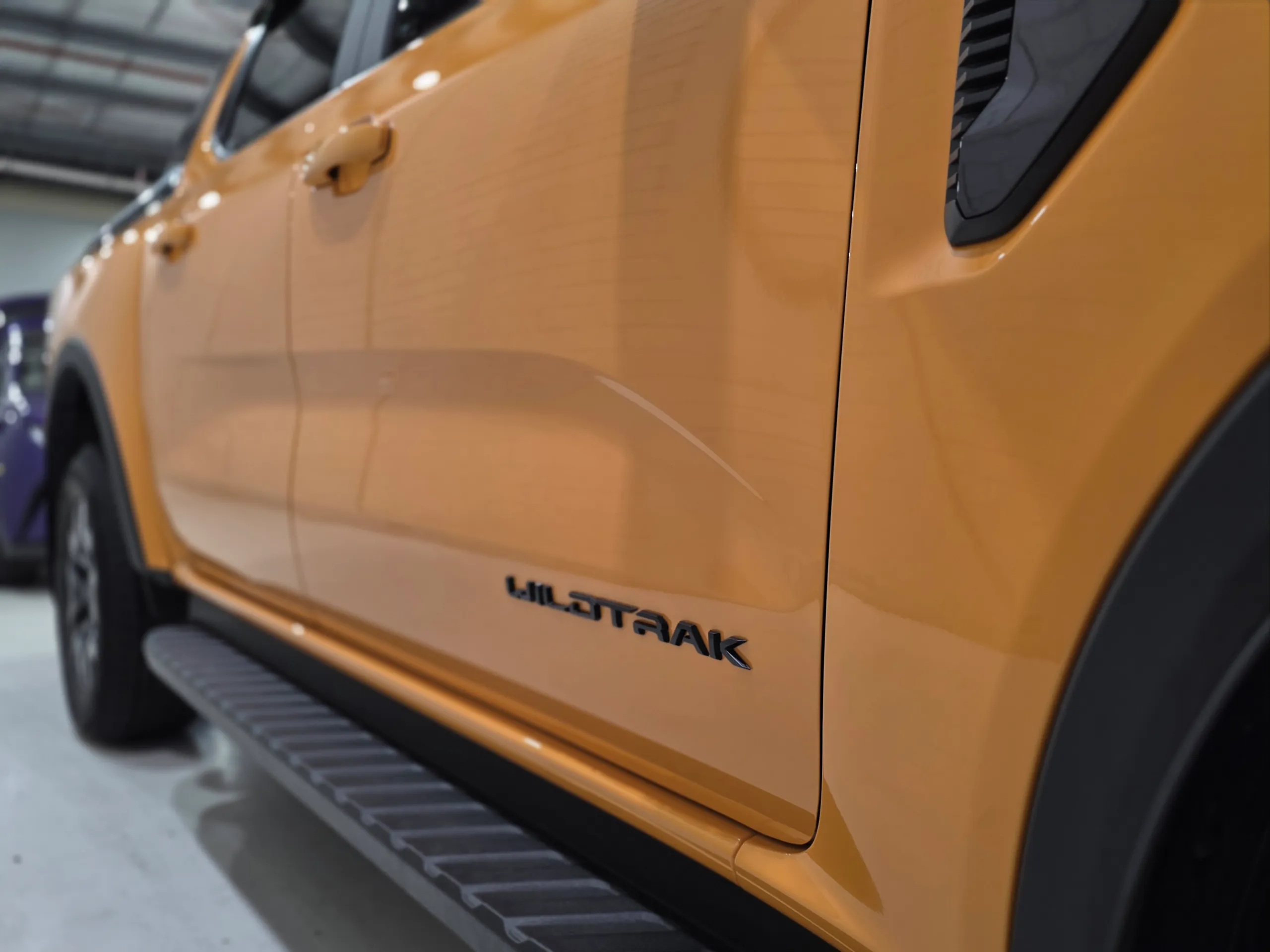 Low-angle view along the orange Ford Ranger doors, showing the Wildtrak badge and side step