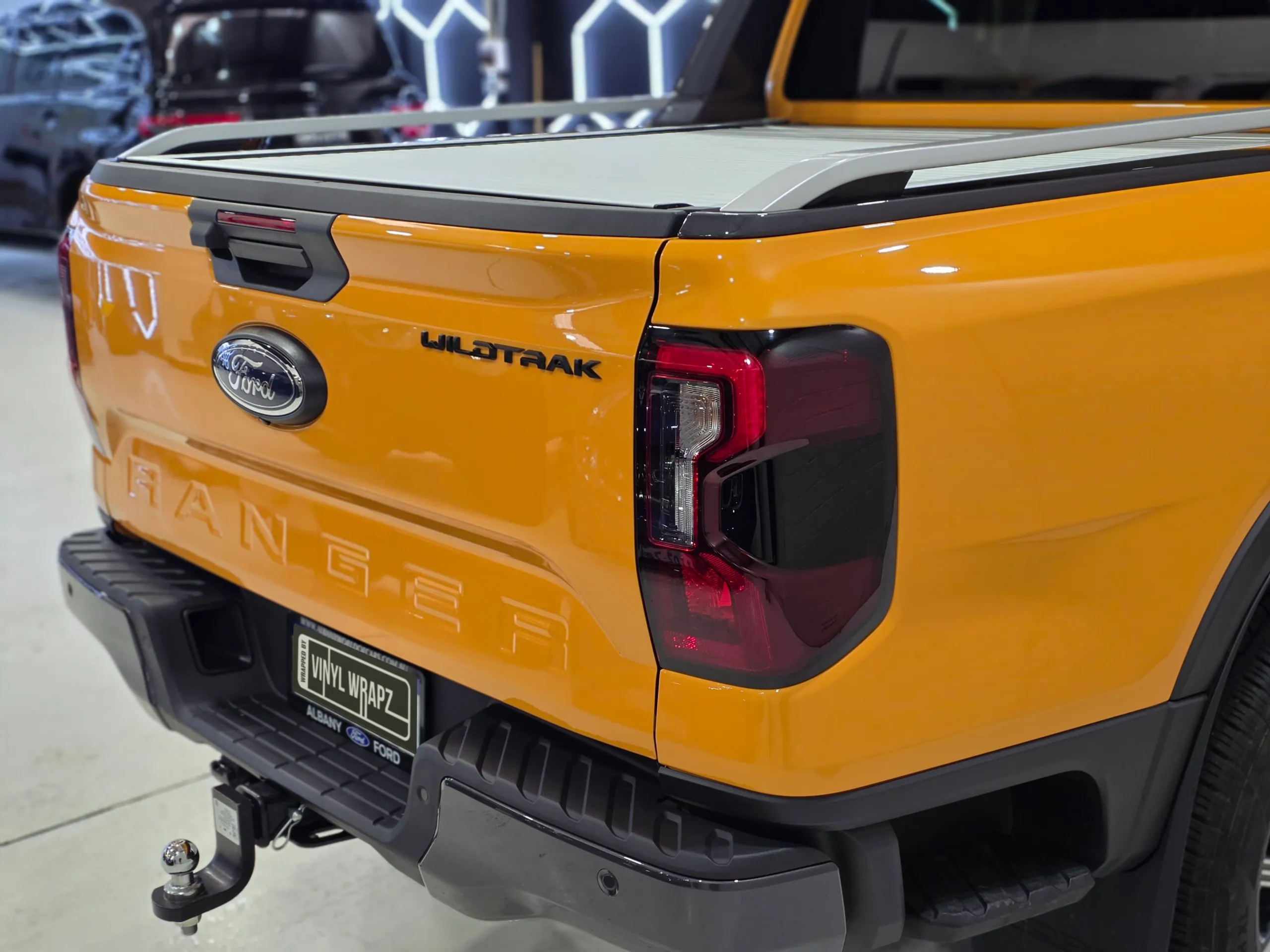 Rear corner of an orange Ford Ranger Wildtrak, with the closed tub cover and tail light