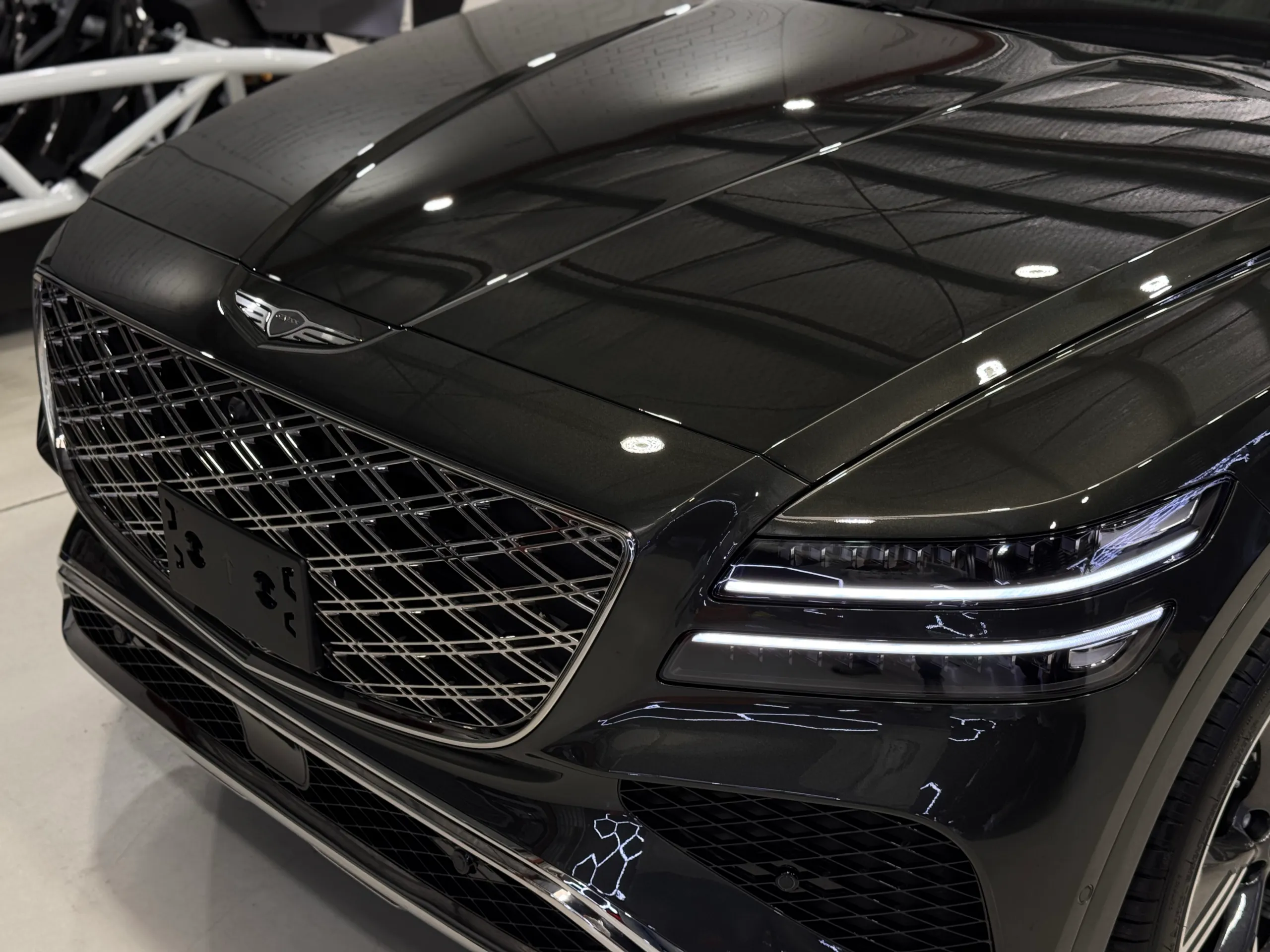 Genesis GV80 grille and headlight beneath a glossy bonnet reflecting the workshop roof