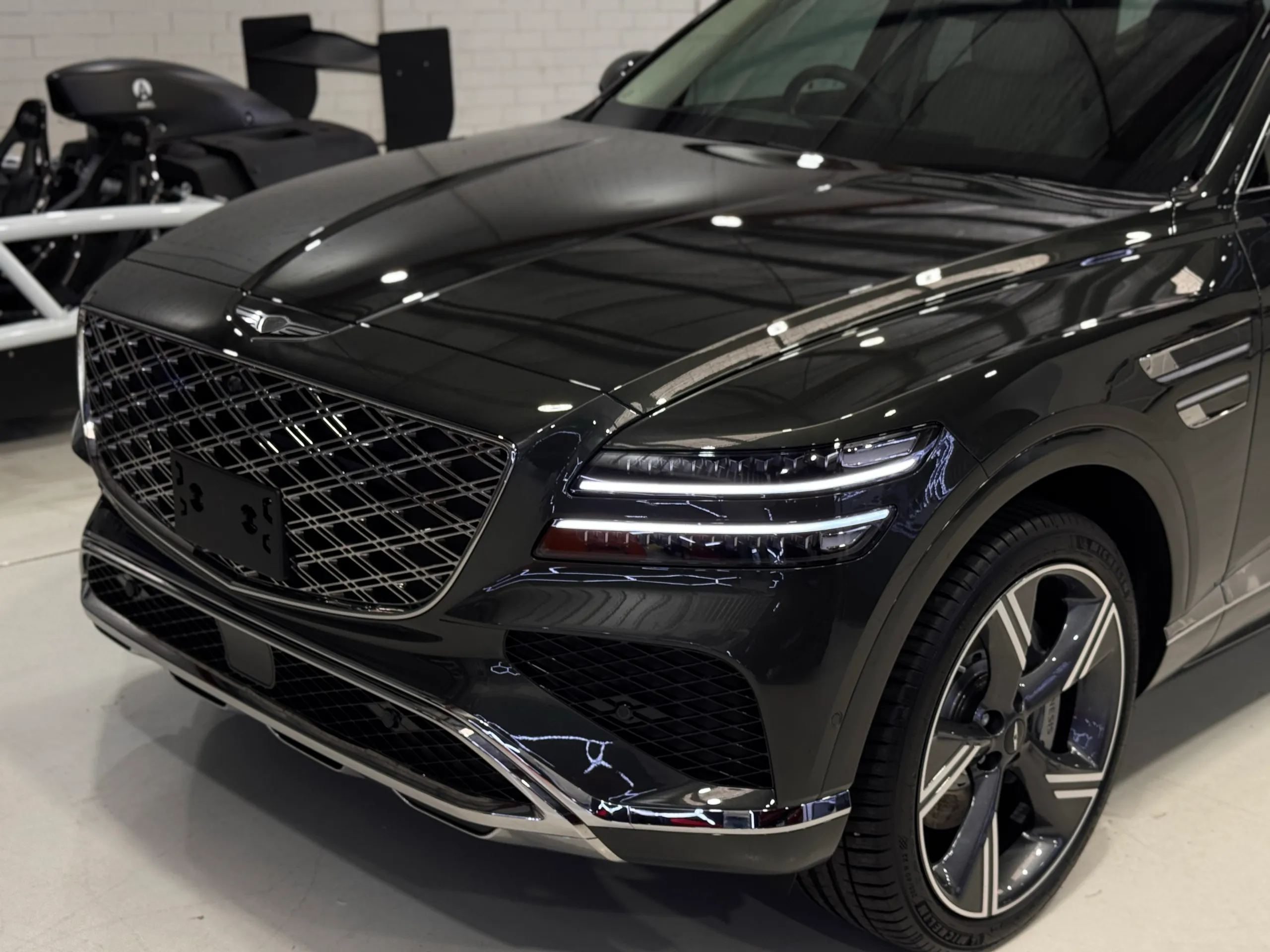 Gloss dark Genesis GV80 front corner, wheel and grille in the workshop