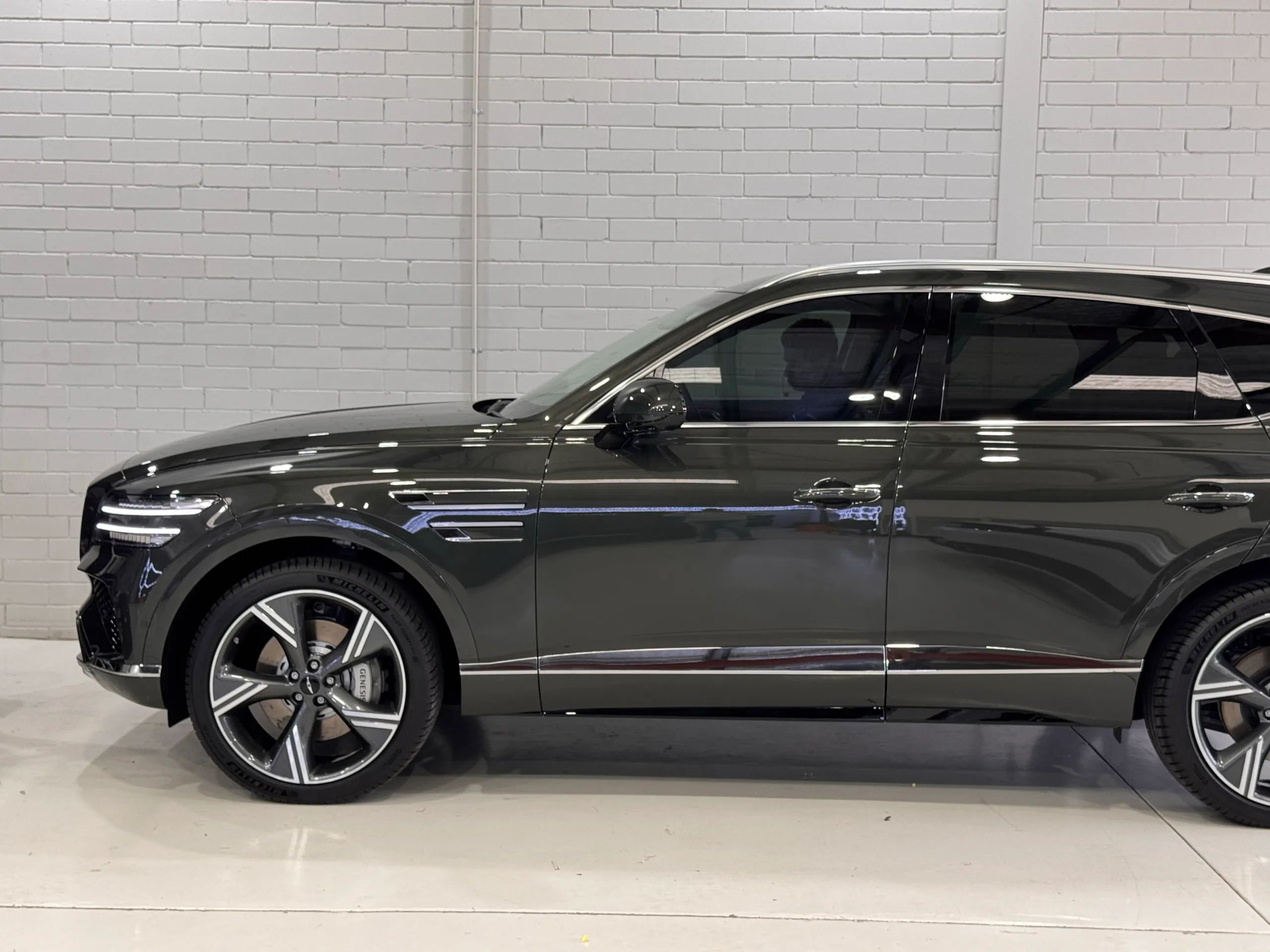 Side view of the Genesis GV80 front wheel and doors against a white workshop wall