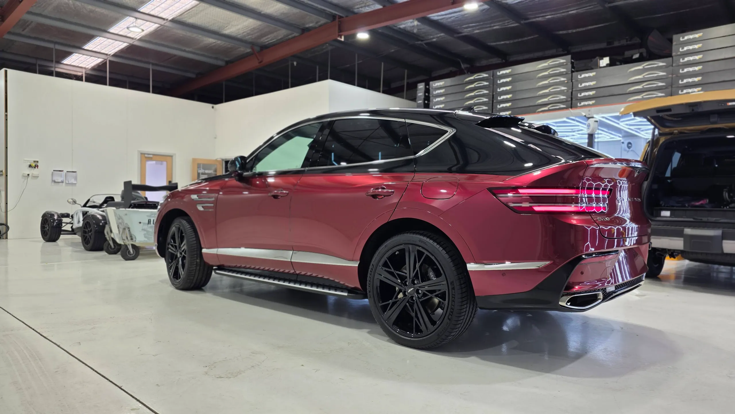 Red and black Genesis GV80 Coupe viewed from the rear in the workshop