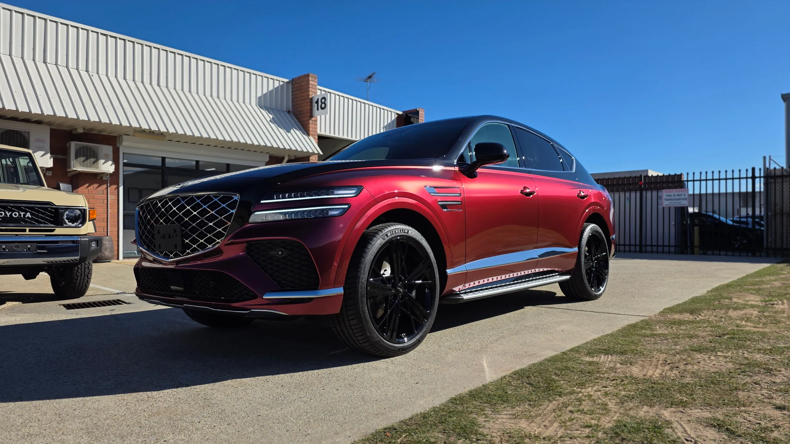 Red and black Genesis GV80 Coupe parked outside the workshop in sunlight
