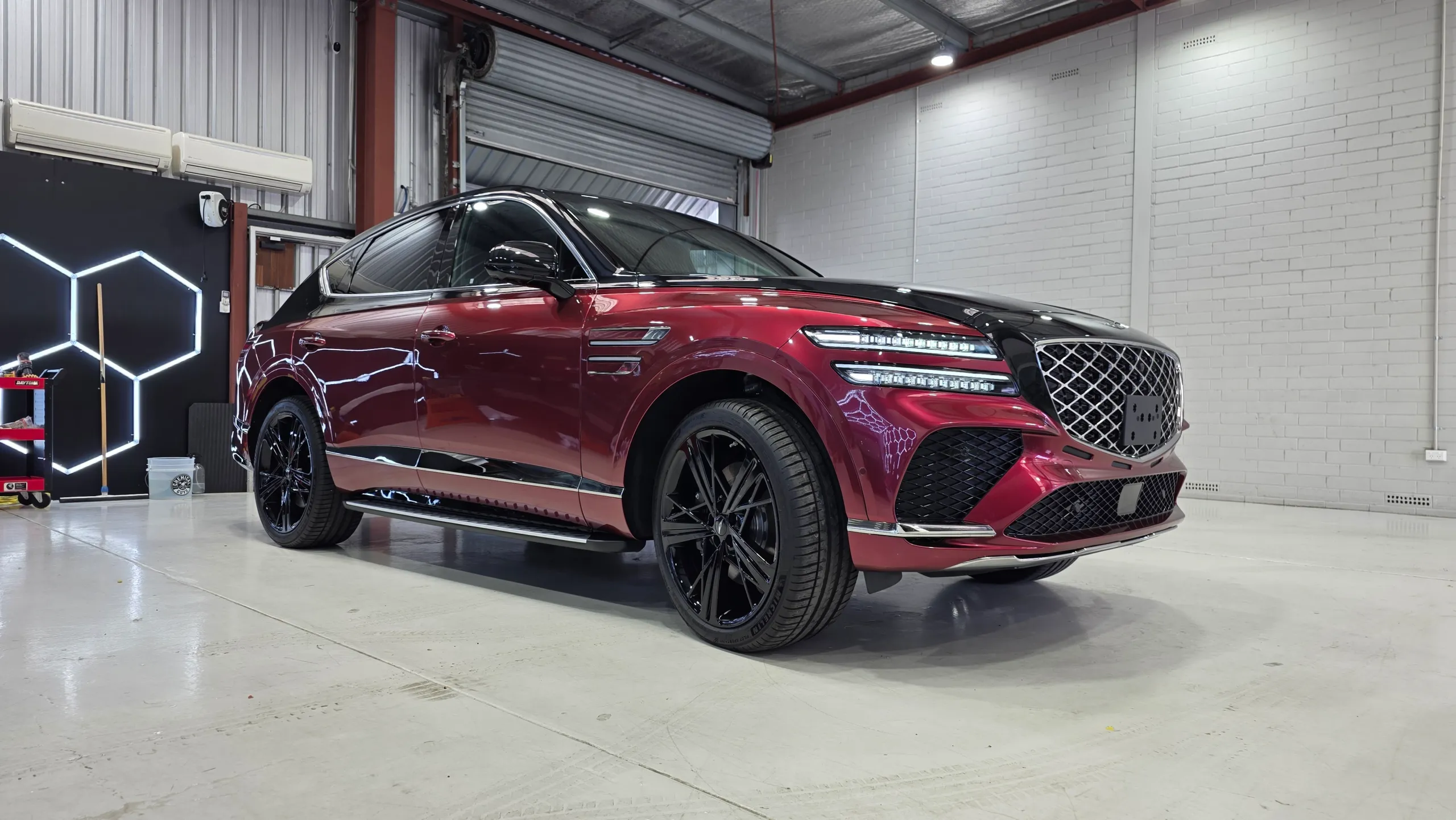 Red and black Genesis GV80 Coupe with black wheels against the workshop wall