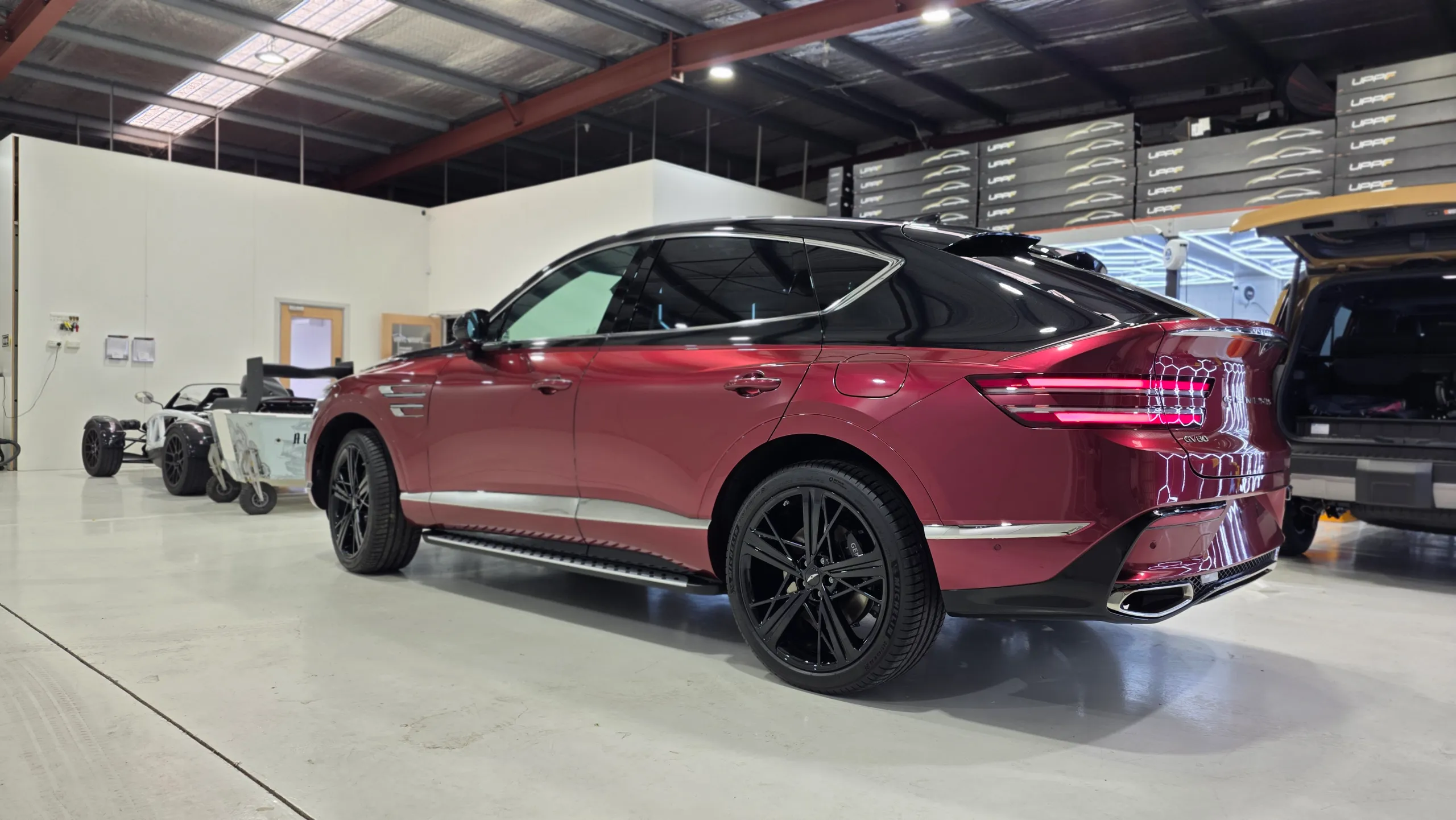 Rear three-quarter view of the red and black Genesis GV80 Coupe in the workshop