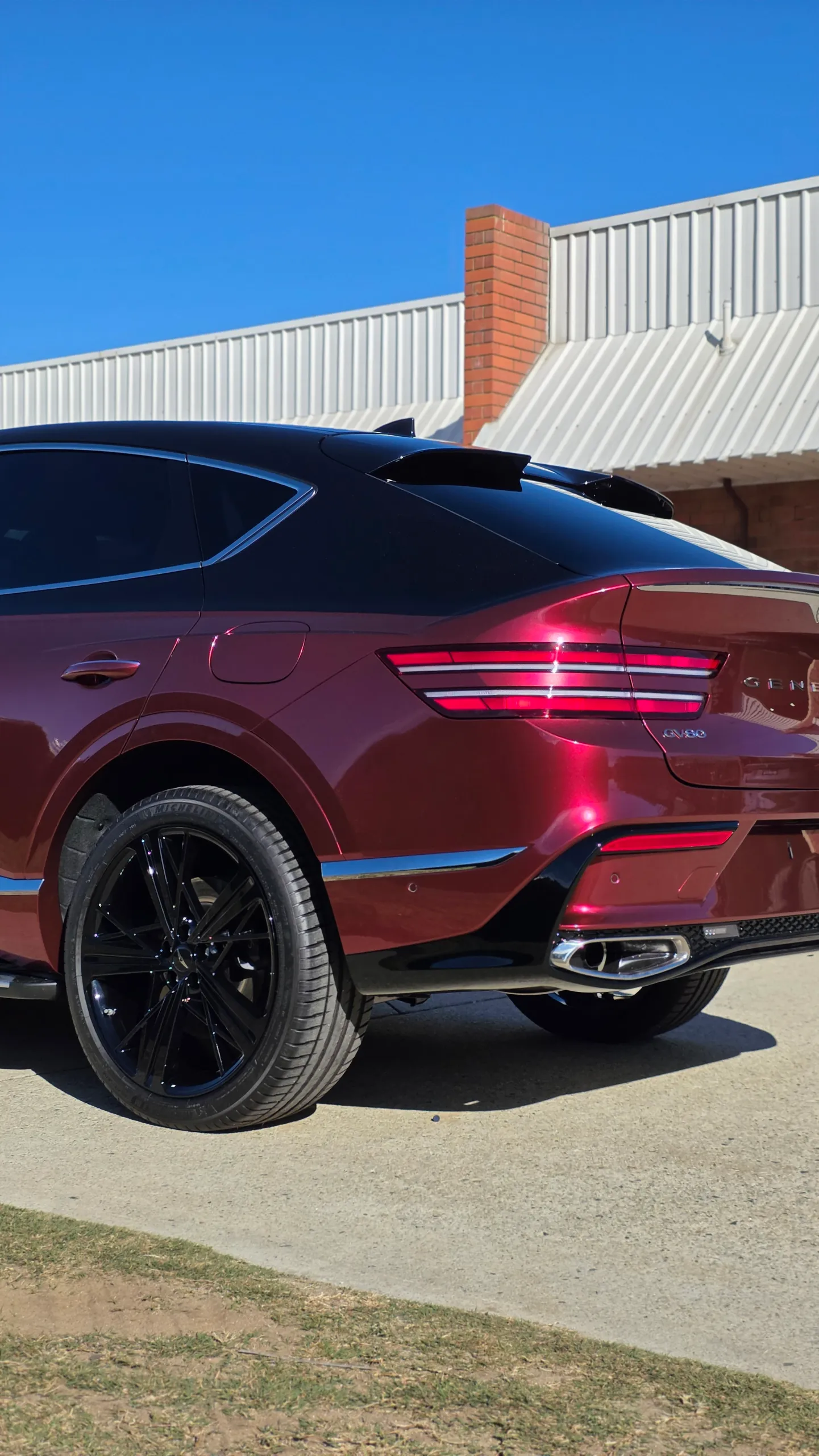 Red Genesis GV80 Coupe rear wheel, tail lights and rear bumper in sunlight