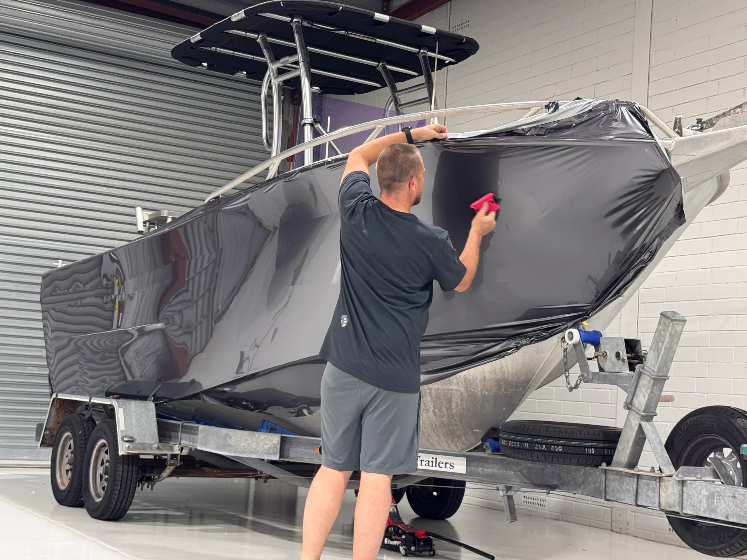 Installer smoothing dark grey film onto the aluminium boat hull