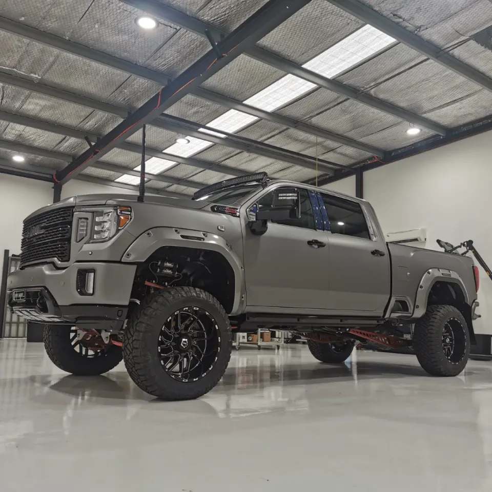 Lifted satin grey GMC Sierra Denali with black off-road wheels and a roof light bar in the workshop