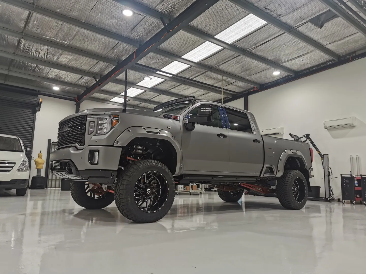 Lifted satin grey GMC Sierra Denali with black off-road wheels and a roof light bar in the workshop
