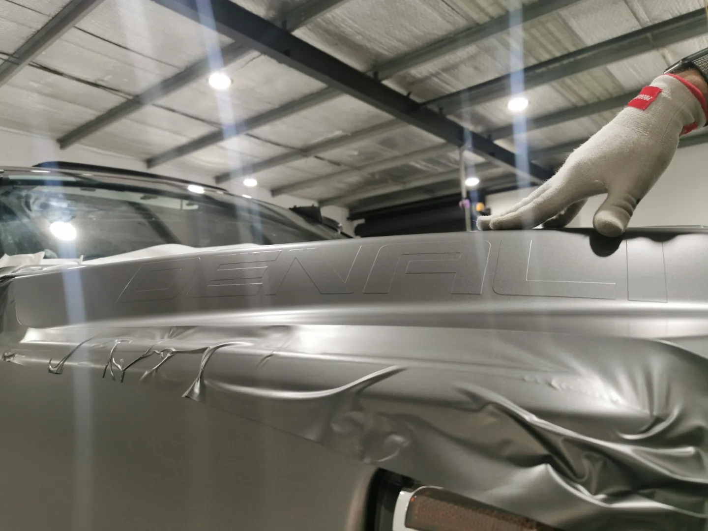 Gloved installer hand fitting grey film around recessed Denali lettering