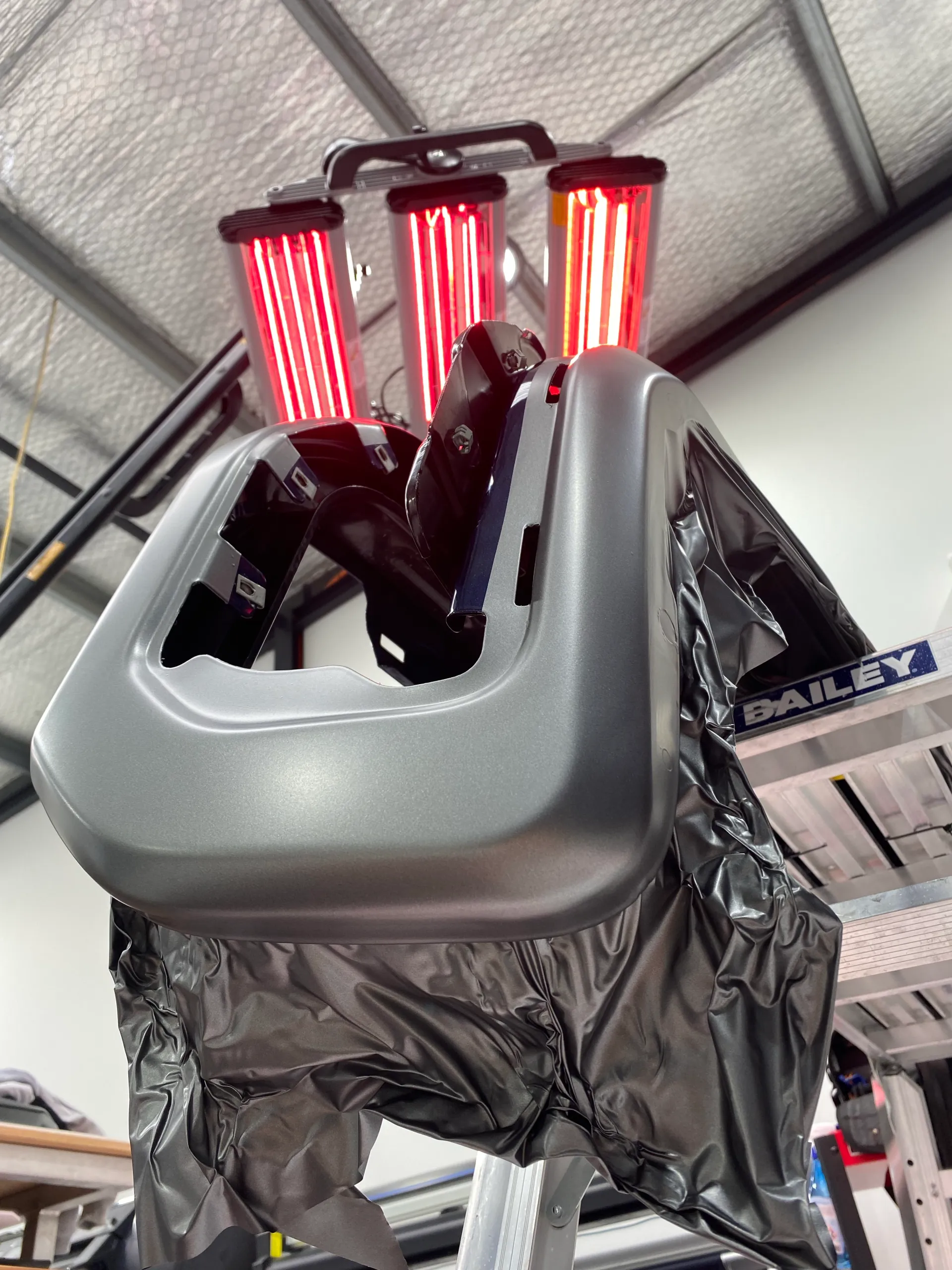 Grey film being heated on a removed GMC bumper component under infrared lamps