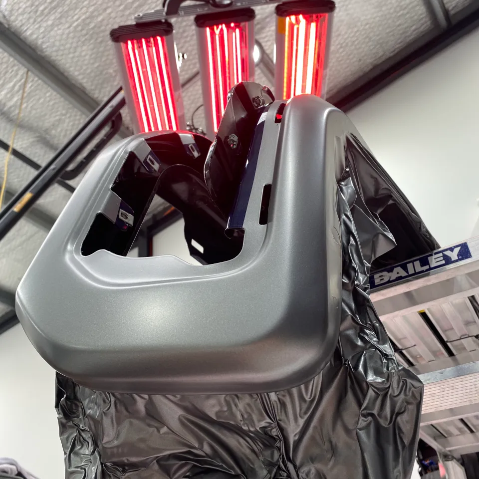 Grey film being heated on a removed GMC bumper component under infrared lamps