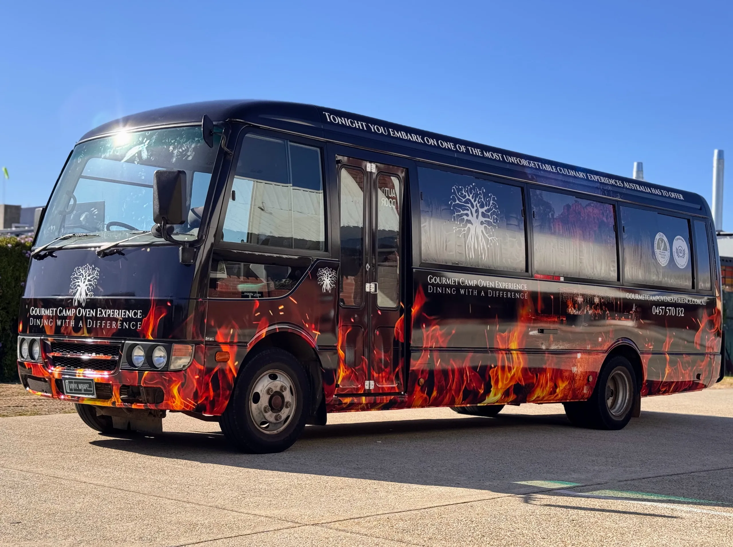 Gourmet Camp Oven Experience bus with orange flame graphics on a dark printed wrap