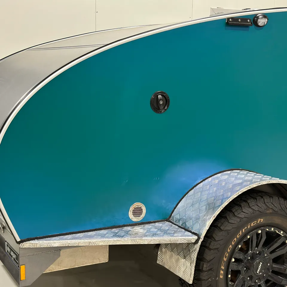 Iridescent green camping trailer side above a black wheel and checkerplate trim