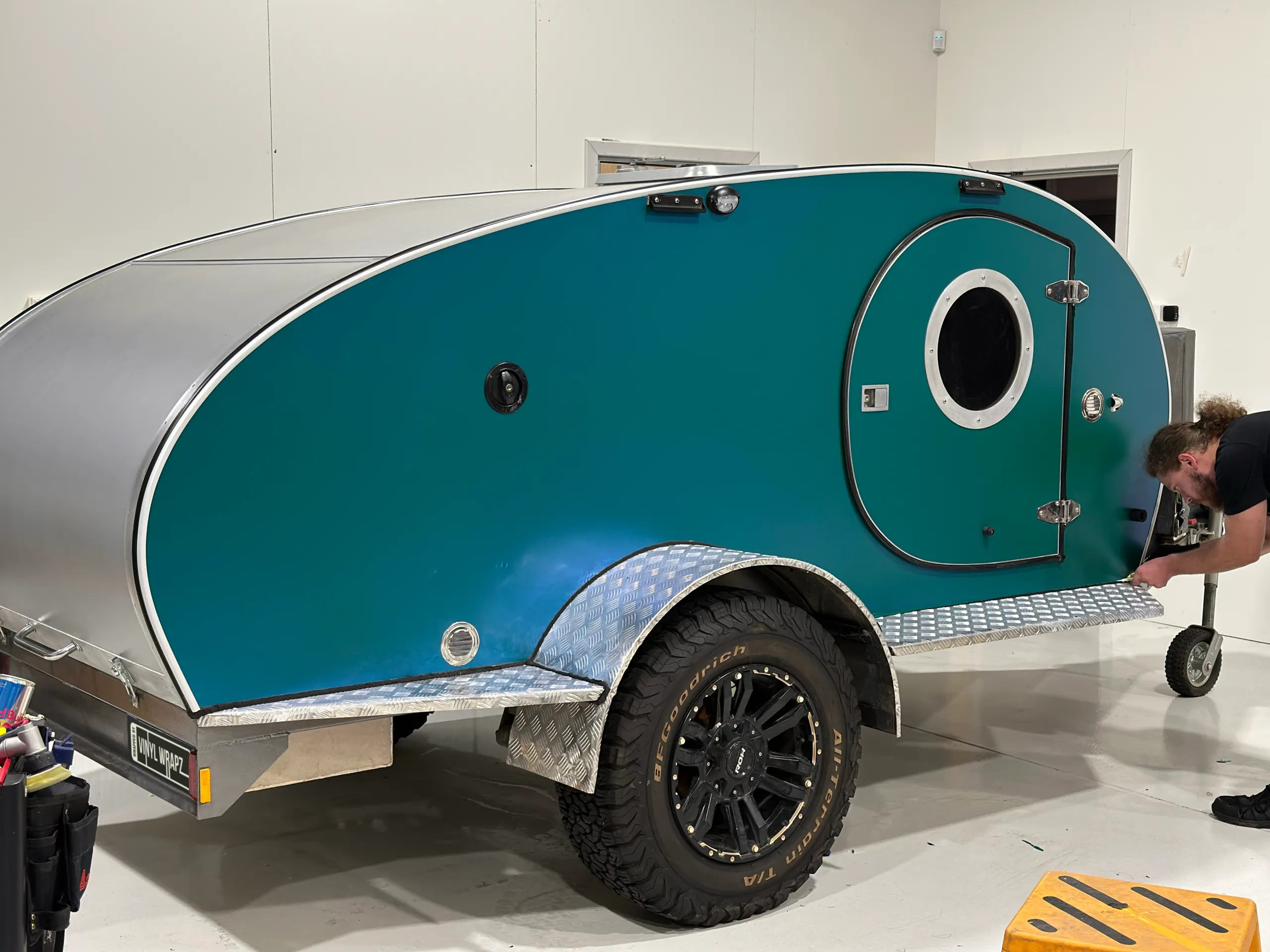 Installer finishing the edge of green colour-shift film on a camping trailer