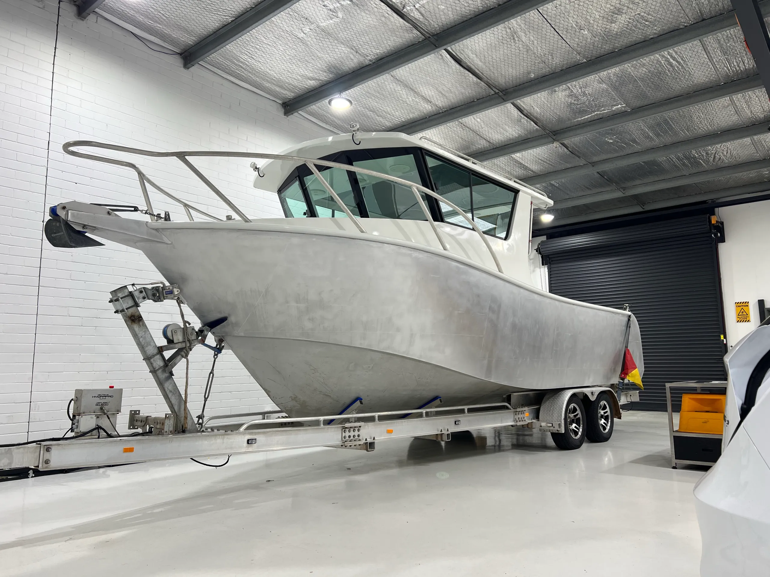 Bare aluminium boat hull with a white cabin on a trailer in the workshop