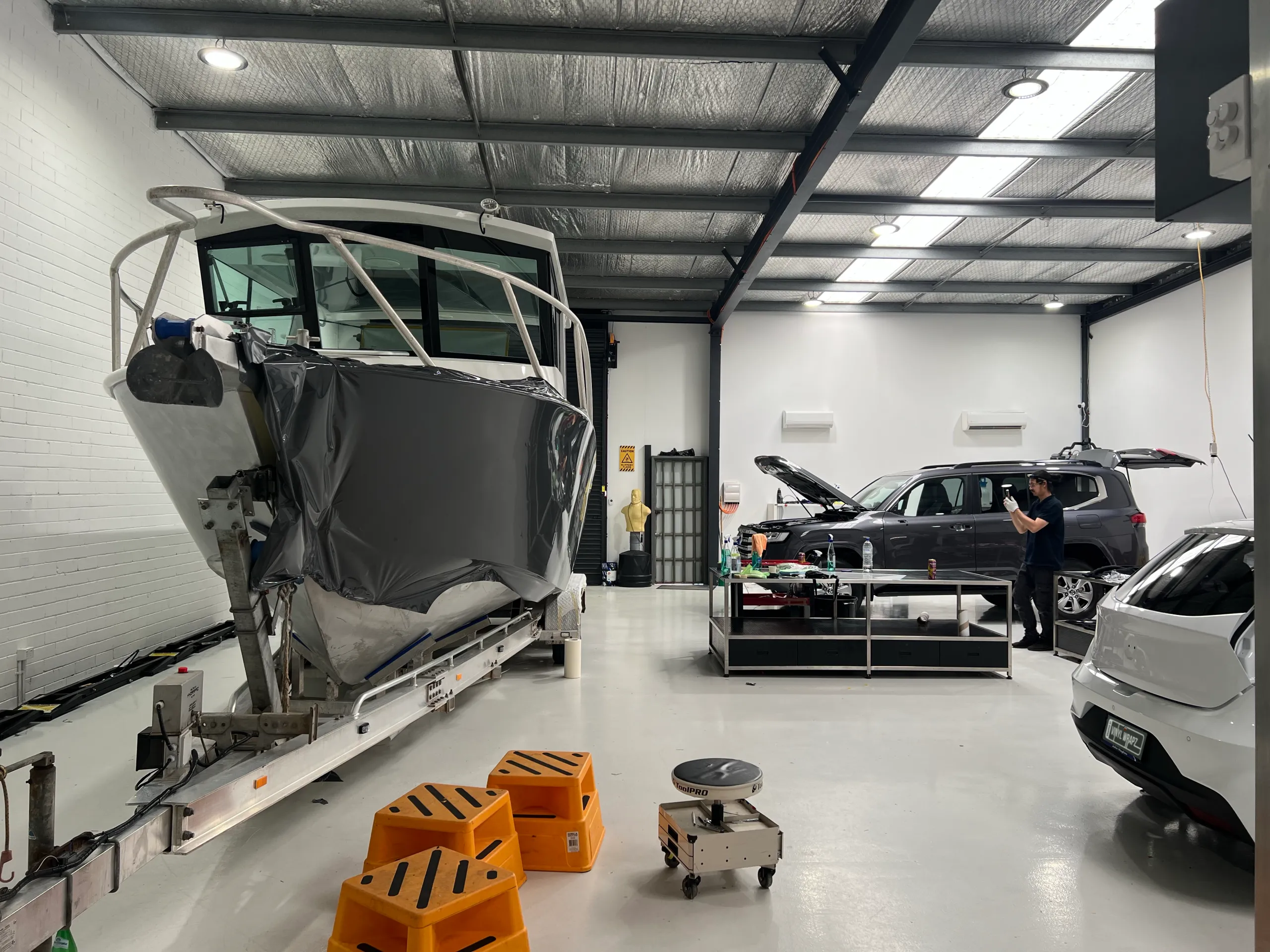 Bow view of the boat during grey film installation, with a person in the workshop background