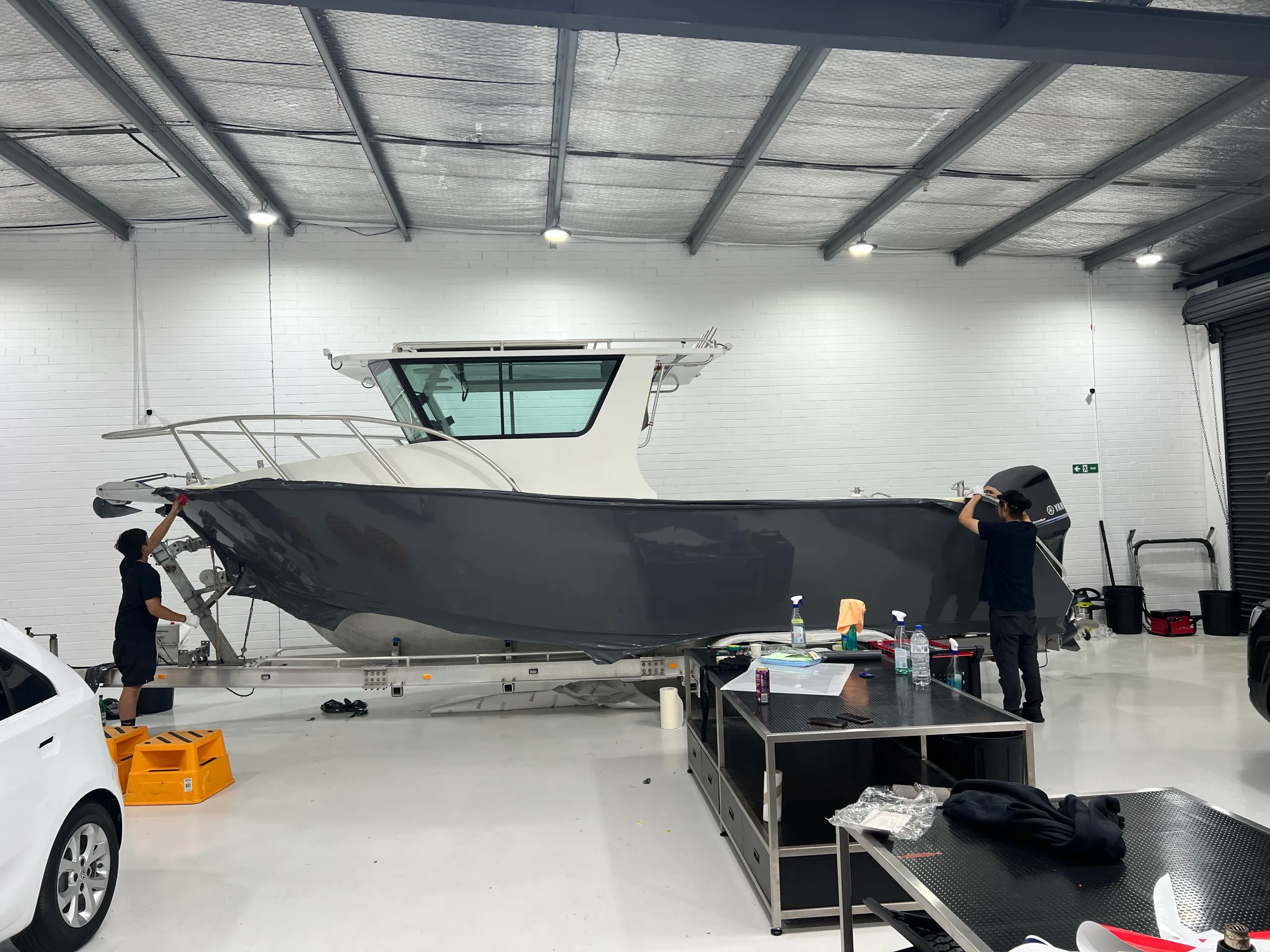 Two installers working at opposite ends of the grey boat hull wrap