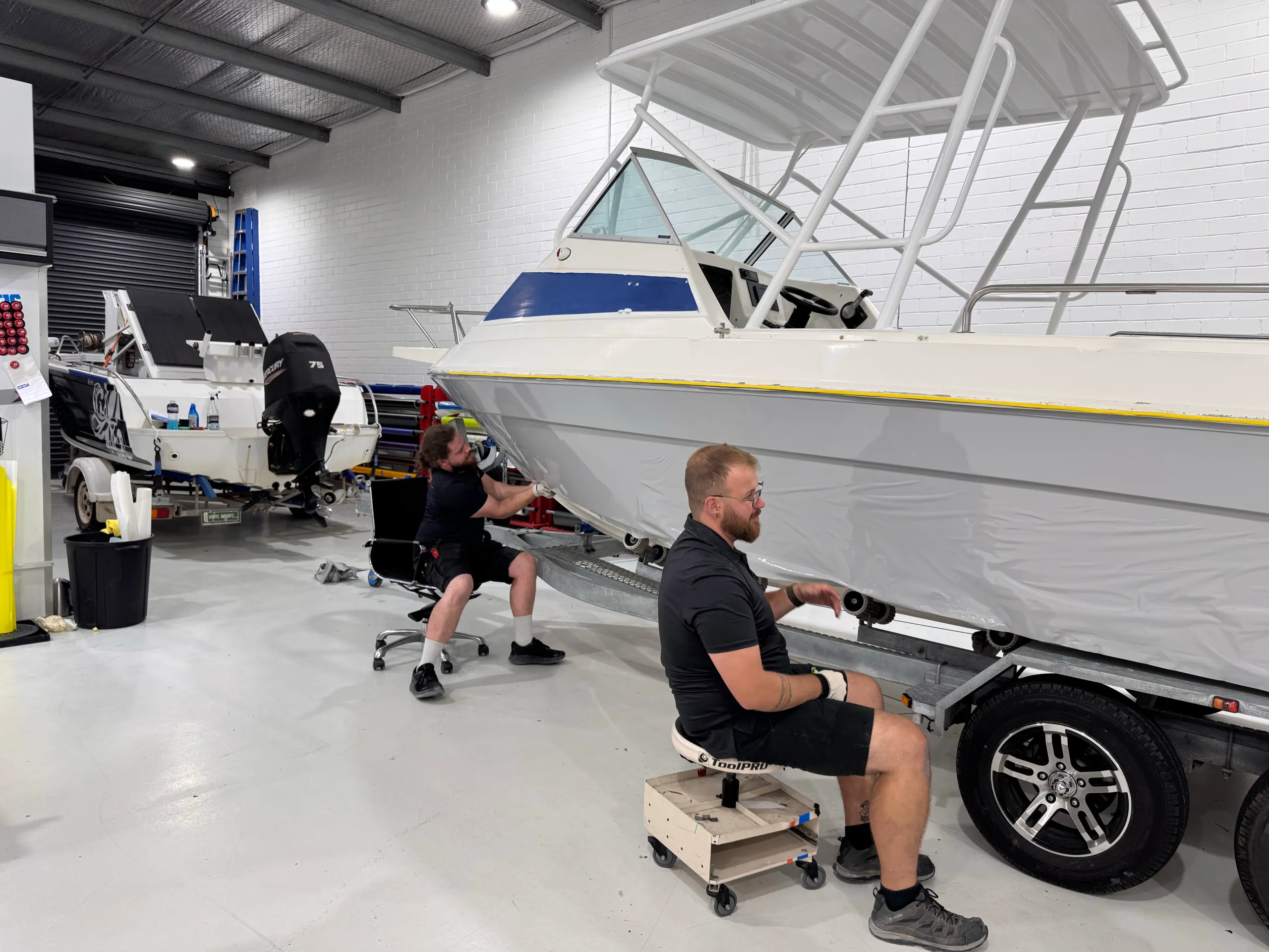 Installers working beside loose grey film on the boat hull