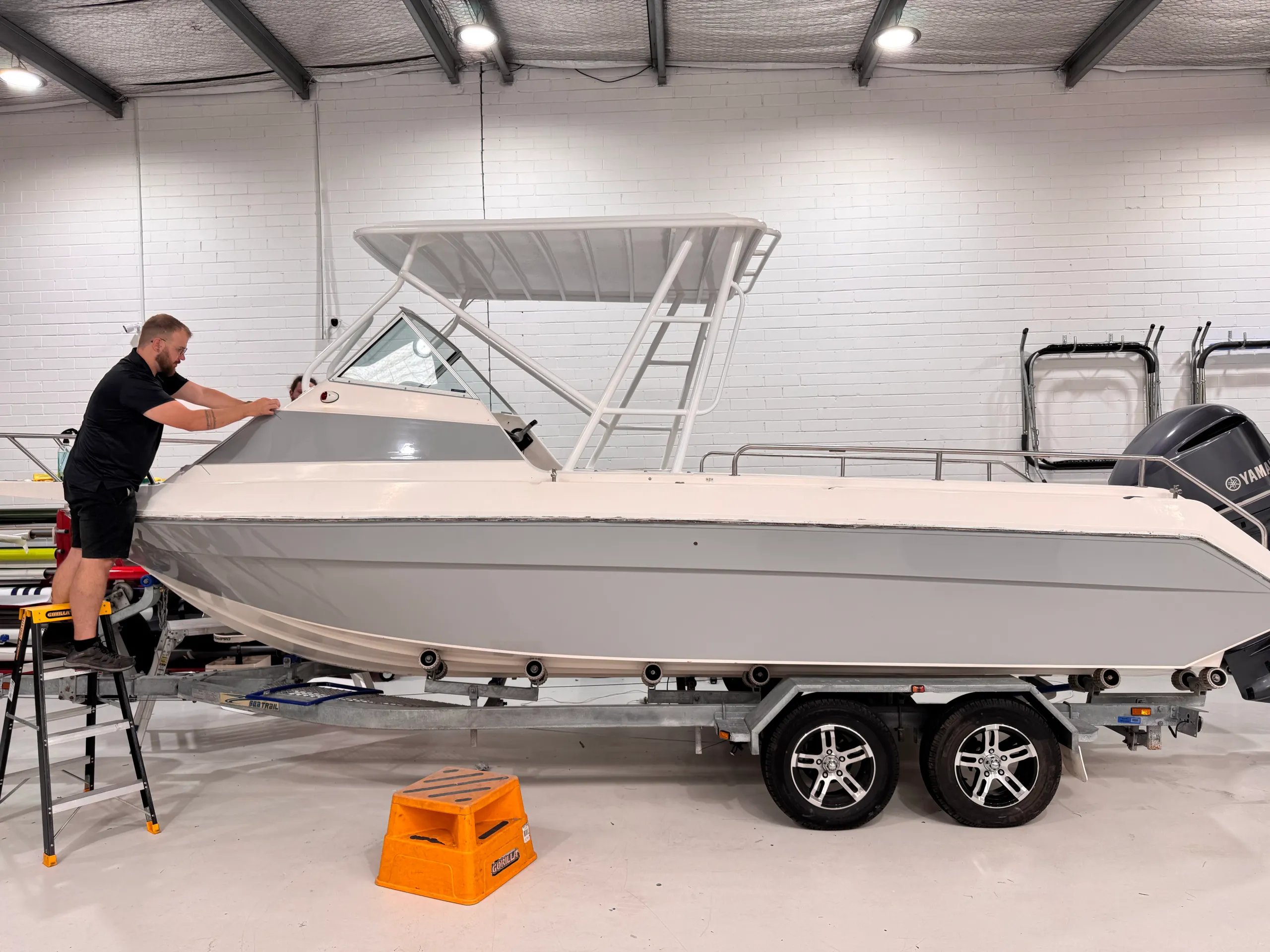 Installer fitting grey film to the boat cabin above the wrapped hull