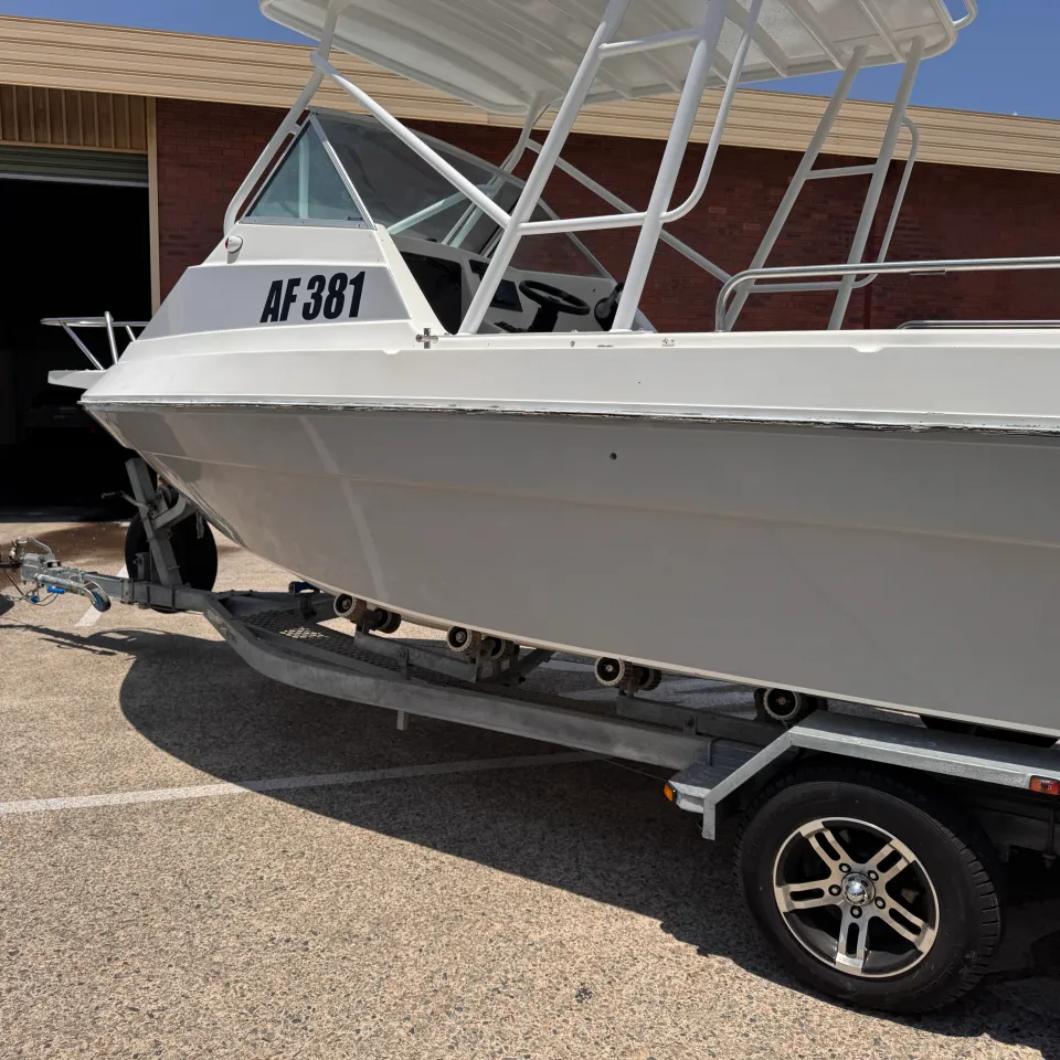 Grey wrapped boat hull beneath a white cabin outside the workshop