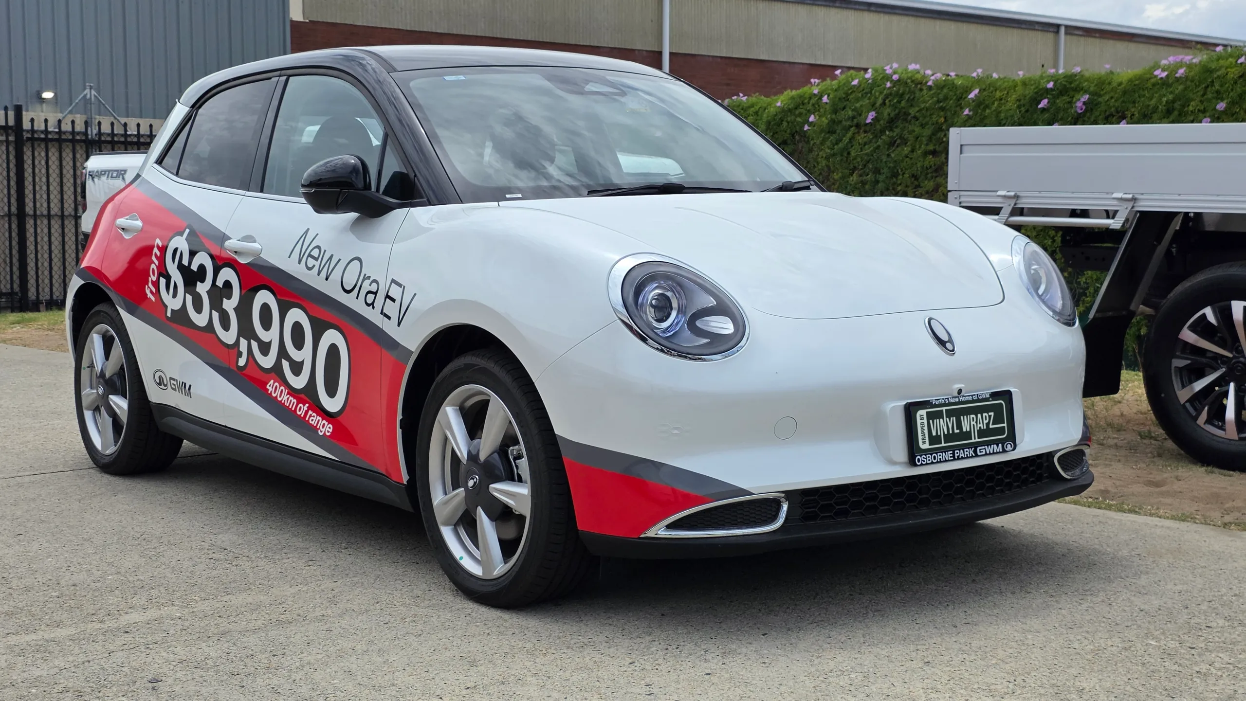 White GWM Ora electric hatchback with red and grey promotional graphics, viewed from the front quarter