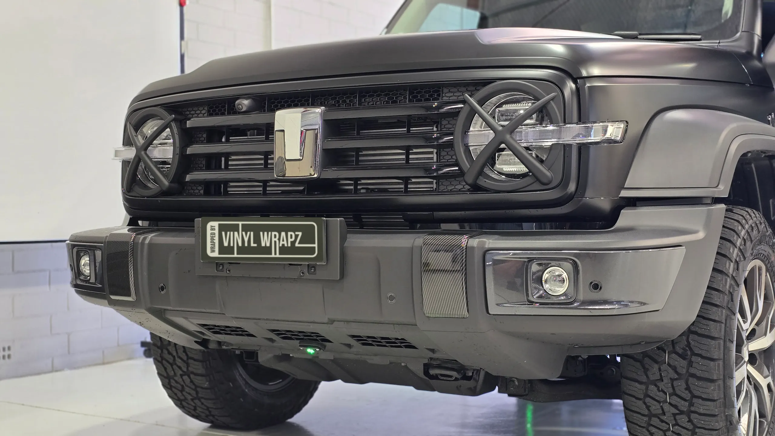 Front of a satin black GWM Tank 300, showing its grille, round headlights and bumper