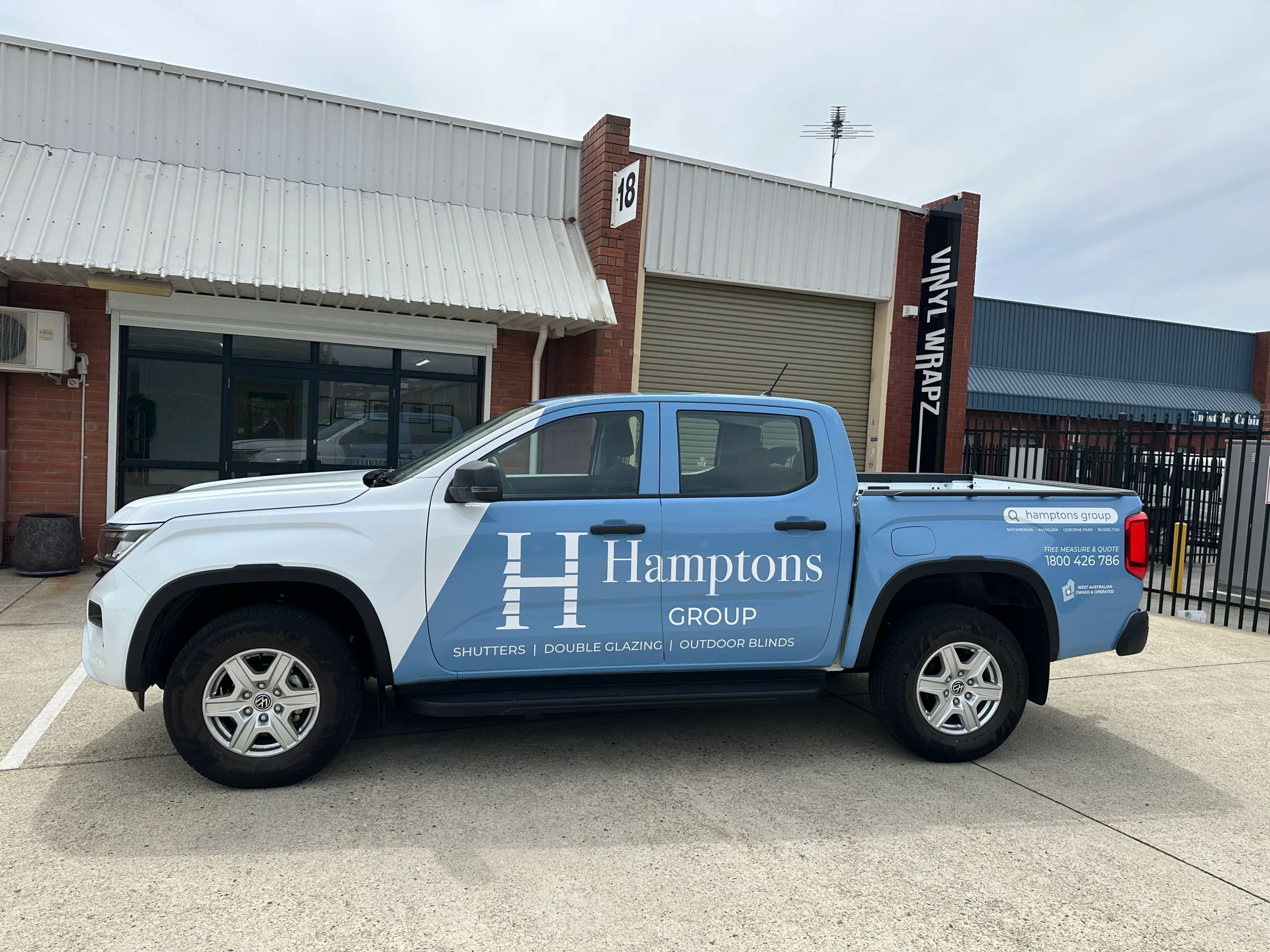 Side view of a Volkswagen Amarok with blue and white Hamptons Group branding outside the workshop