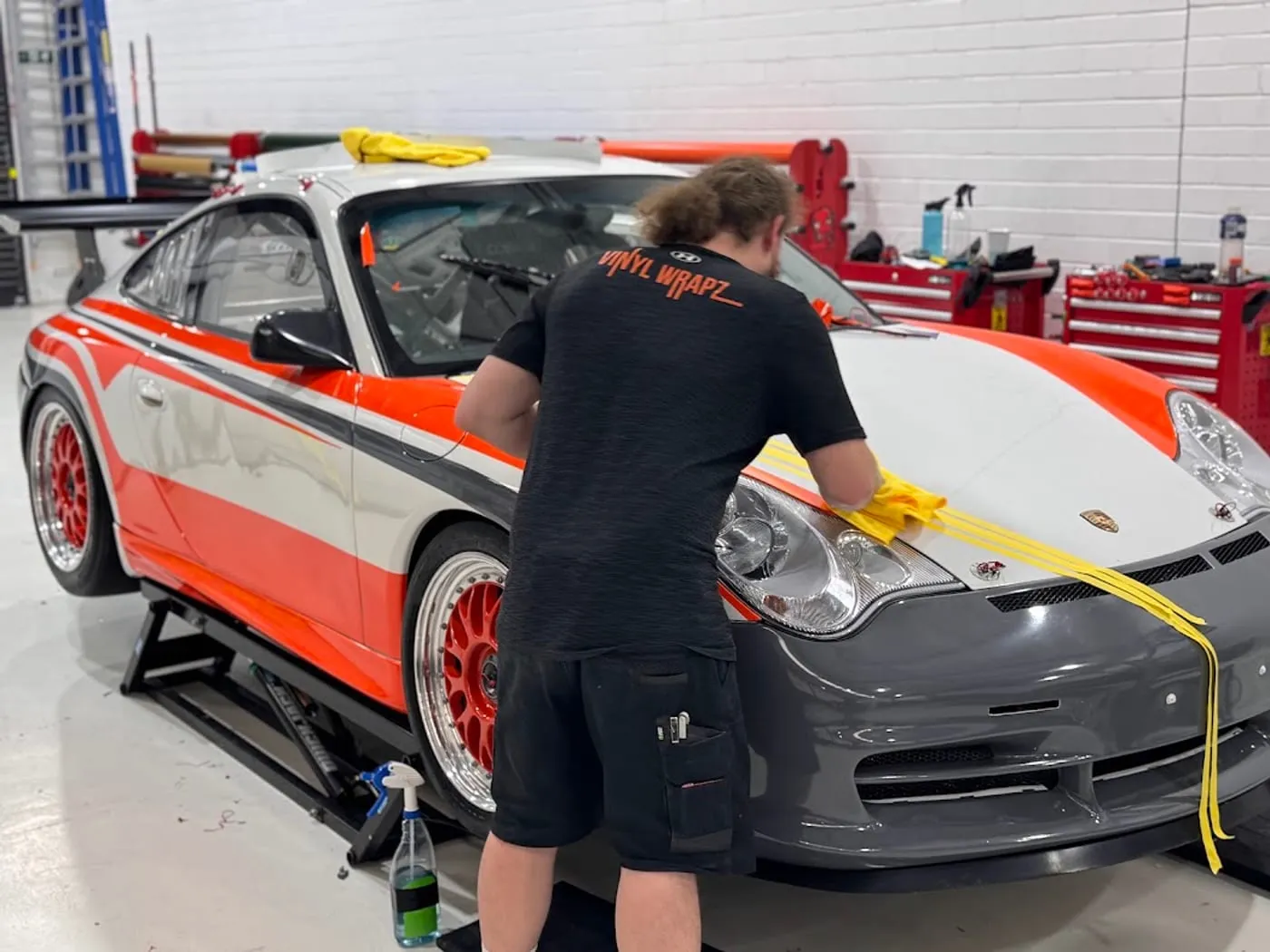 Installer in a Vinyl Wrapz shirt giving a finished Porsche race livery its final wipe-down