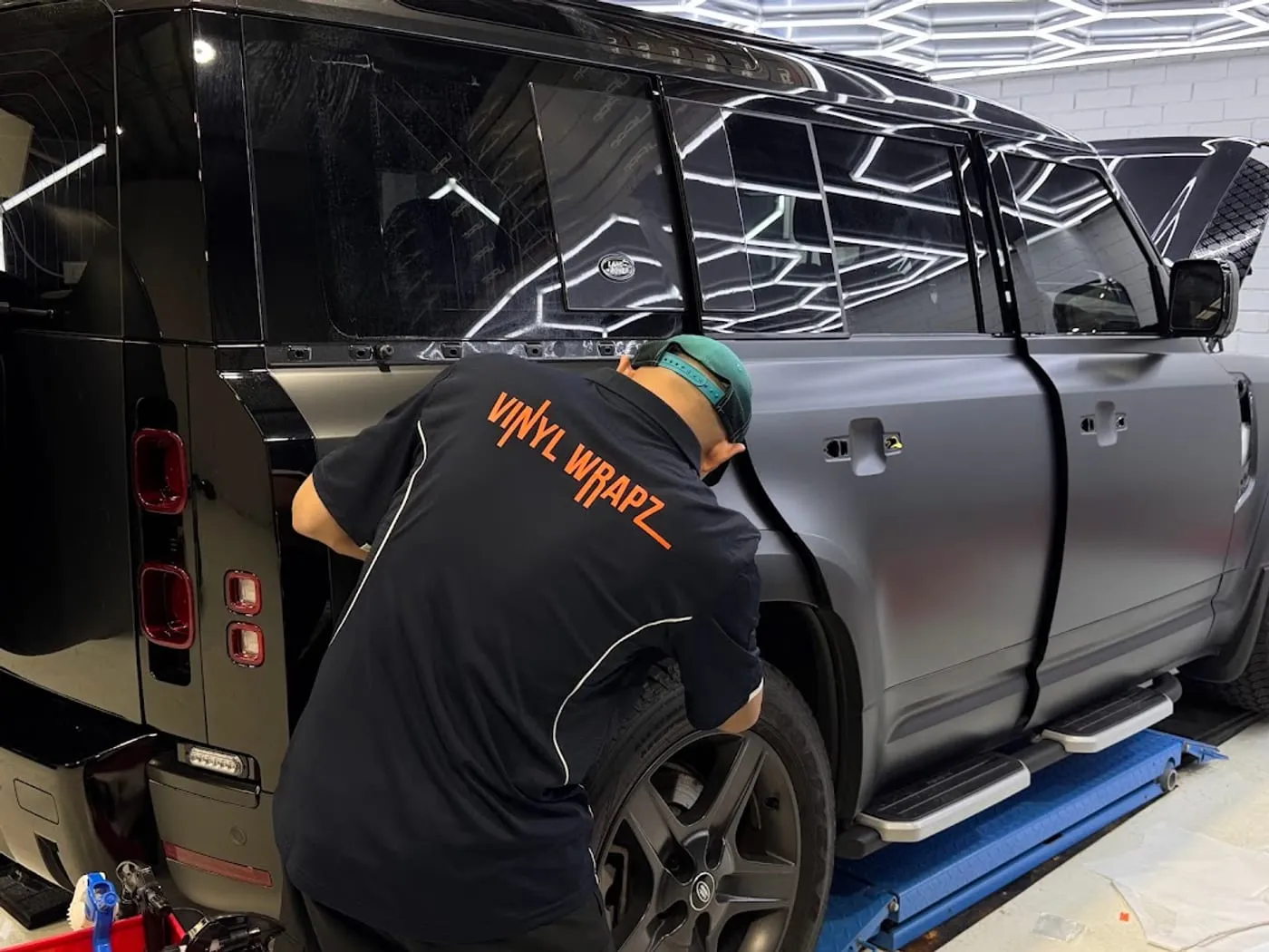 Installer fitting satin grey film to a Land Rover Defender on the hoist
