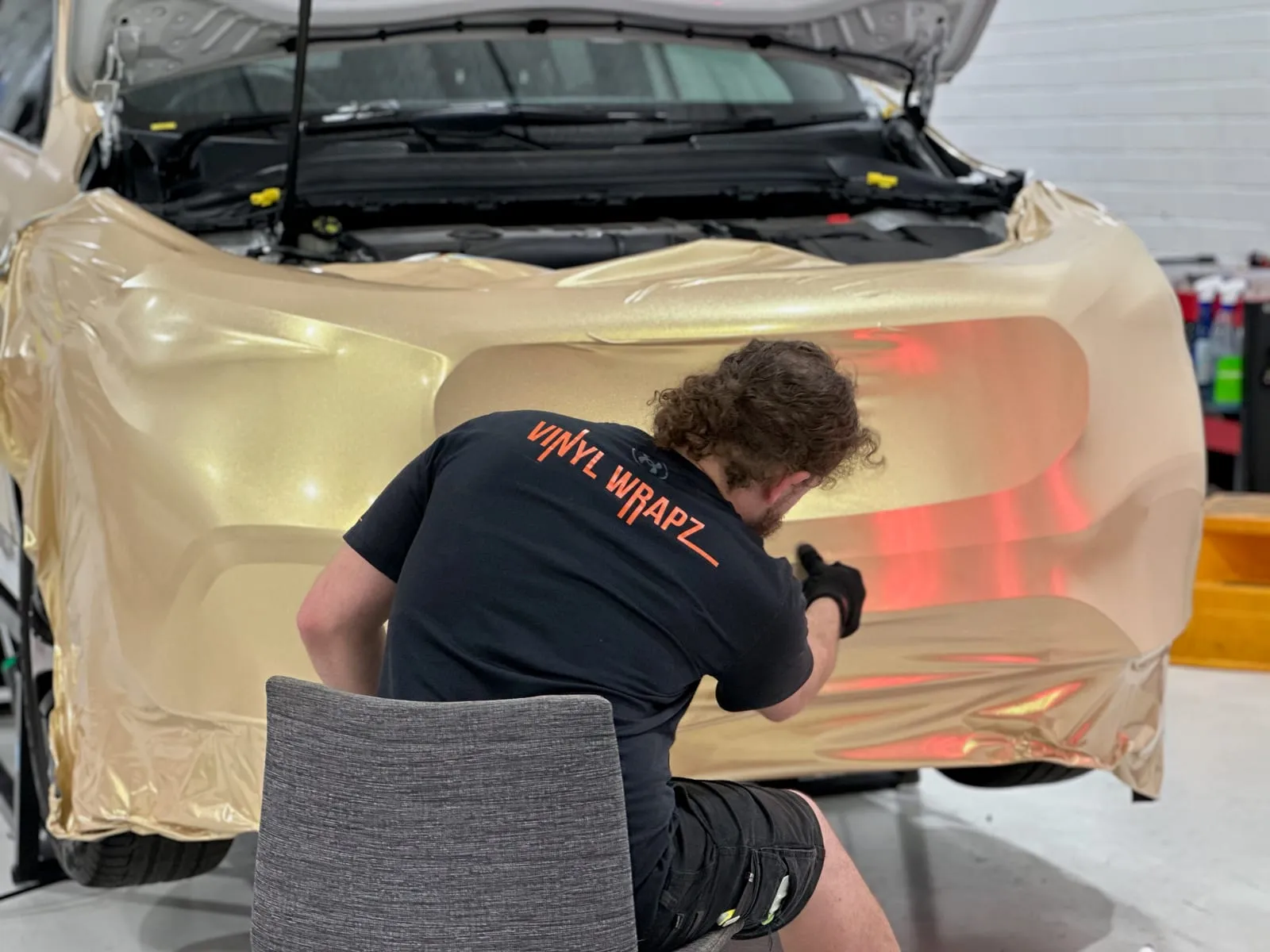 Installer shaping gold metallic colour change film around a bumper with a heat gun