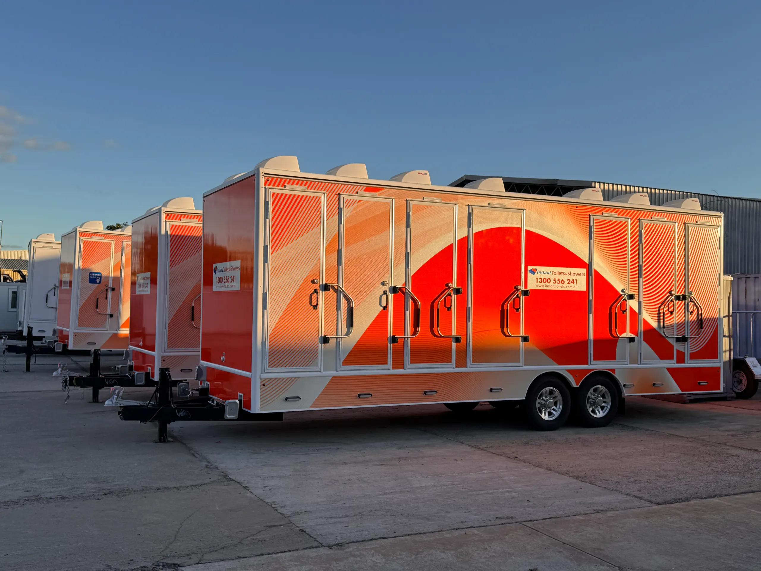 Orange and white amenities trailers lined up outdoors in warm evening light
