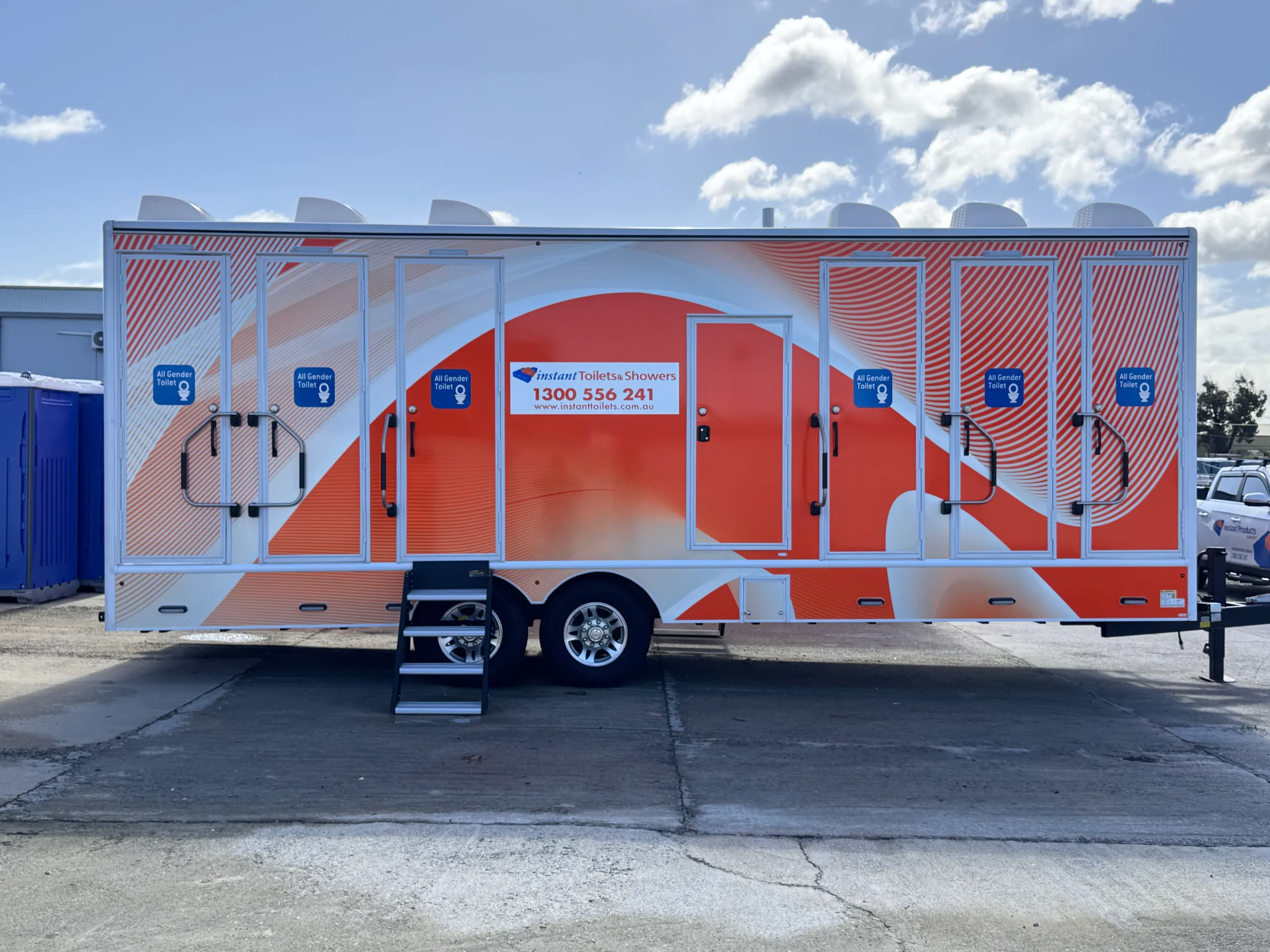 Side profile of an Instant Toilets & Showers trailer with orange graphics, multiple doors and access steps