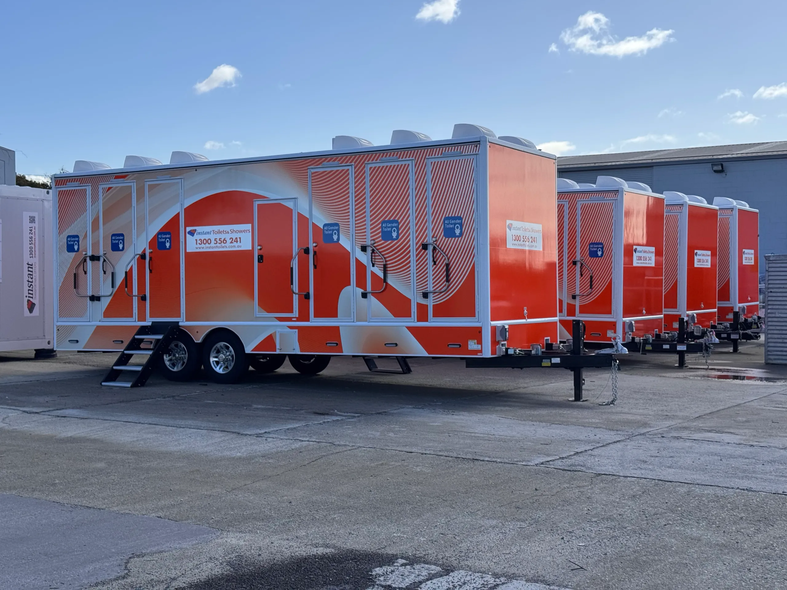 Line of orange and white Instant Toilets & Showers trailers parked outside