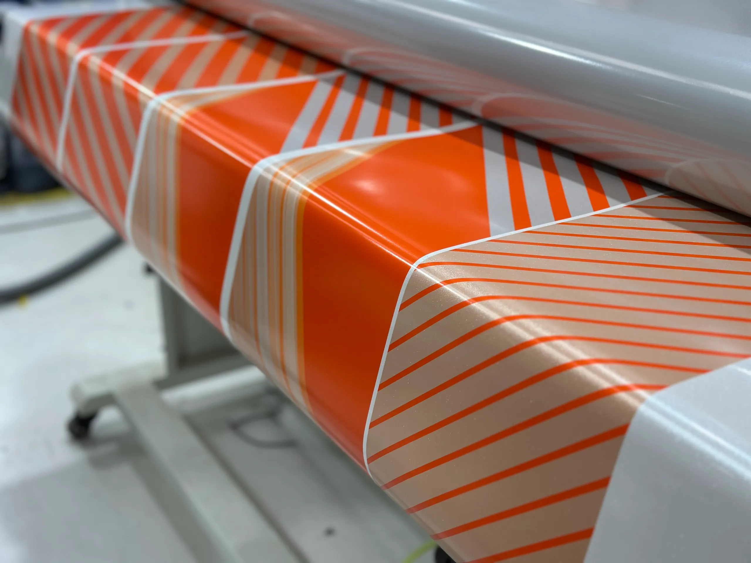 Close-up of orange and white printed wrap film passing over a workshop roller