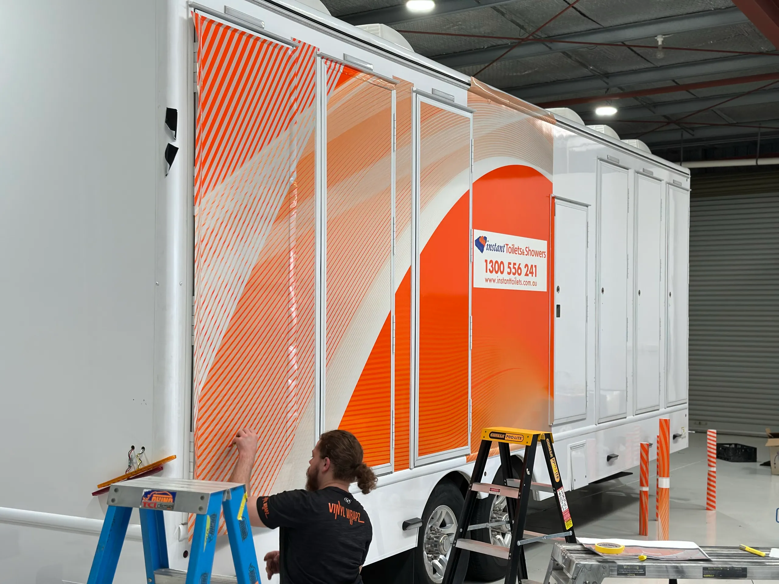 Installer applying orange striped graphics to an Instant Toilets & Showers trailer door panel