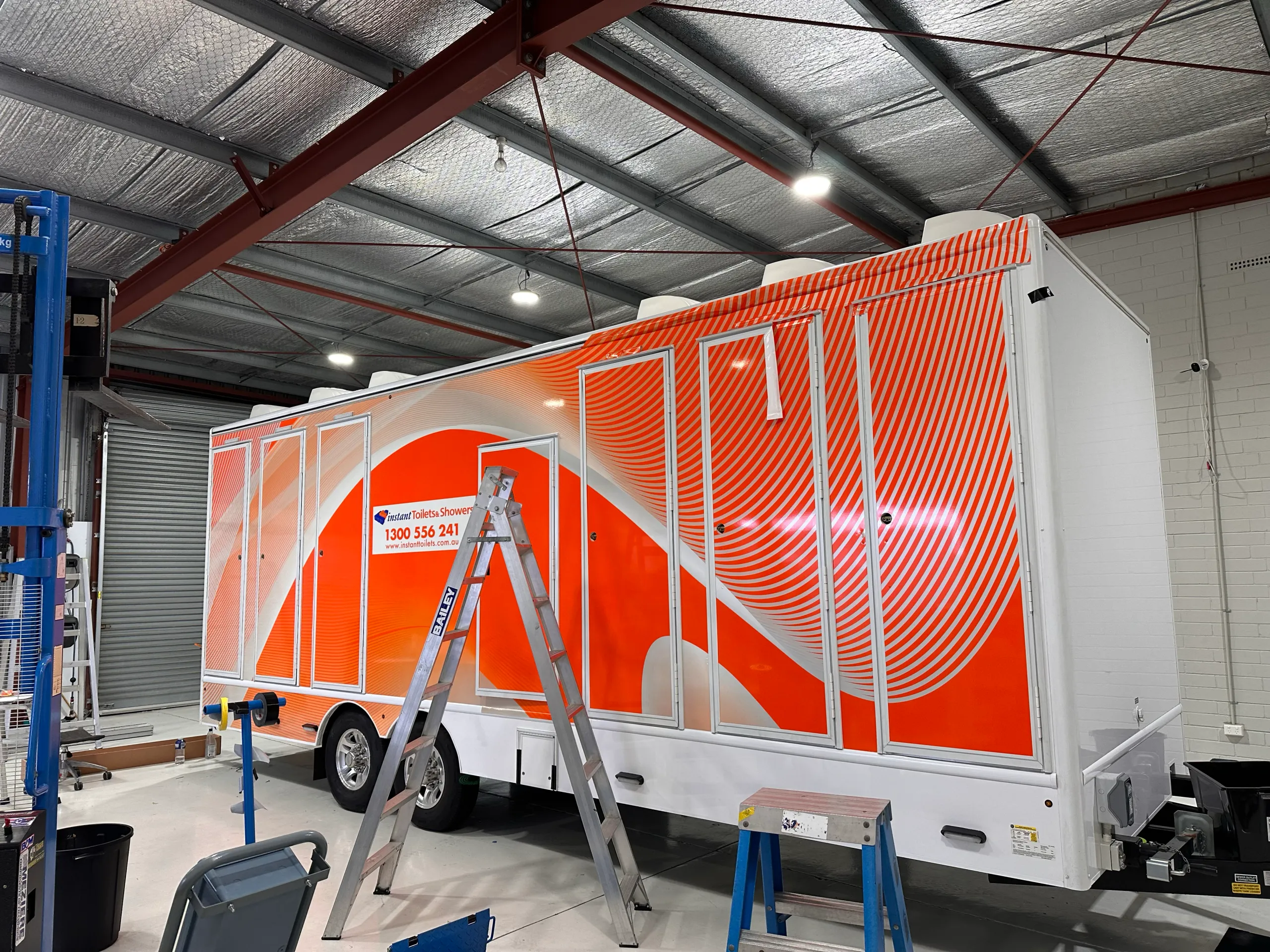 Orange and white trailer graphics during installation, with access ladders and unfinished door hardware