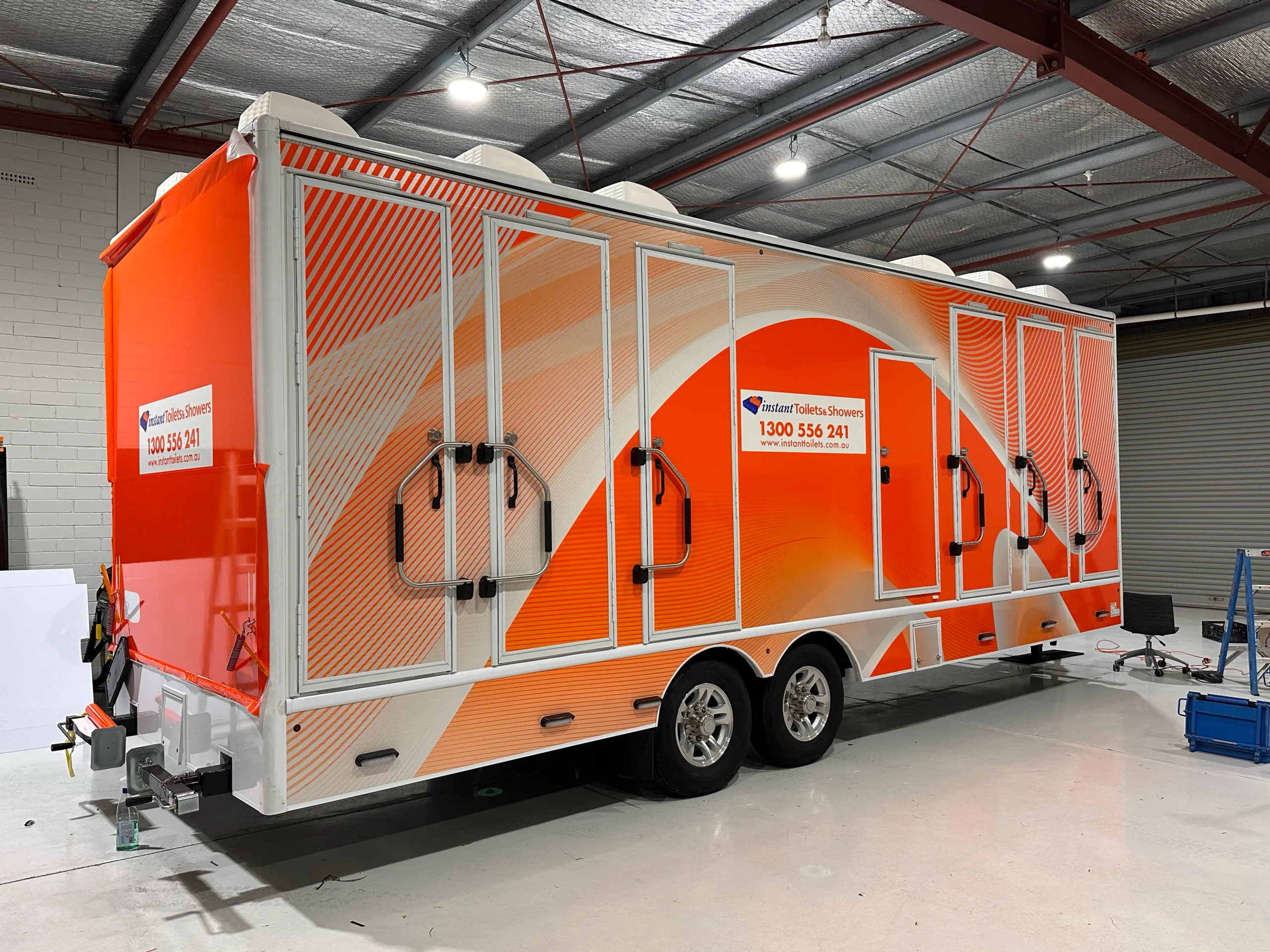 Instant Toilets & Showers trailer in the workshop with orange graphics and loose film along the upper edge