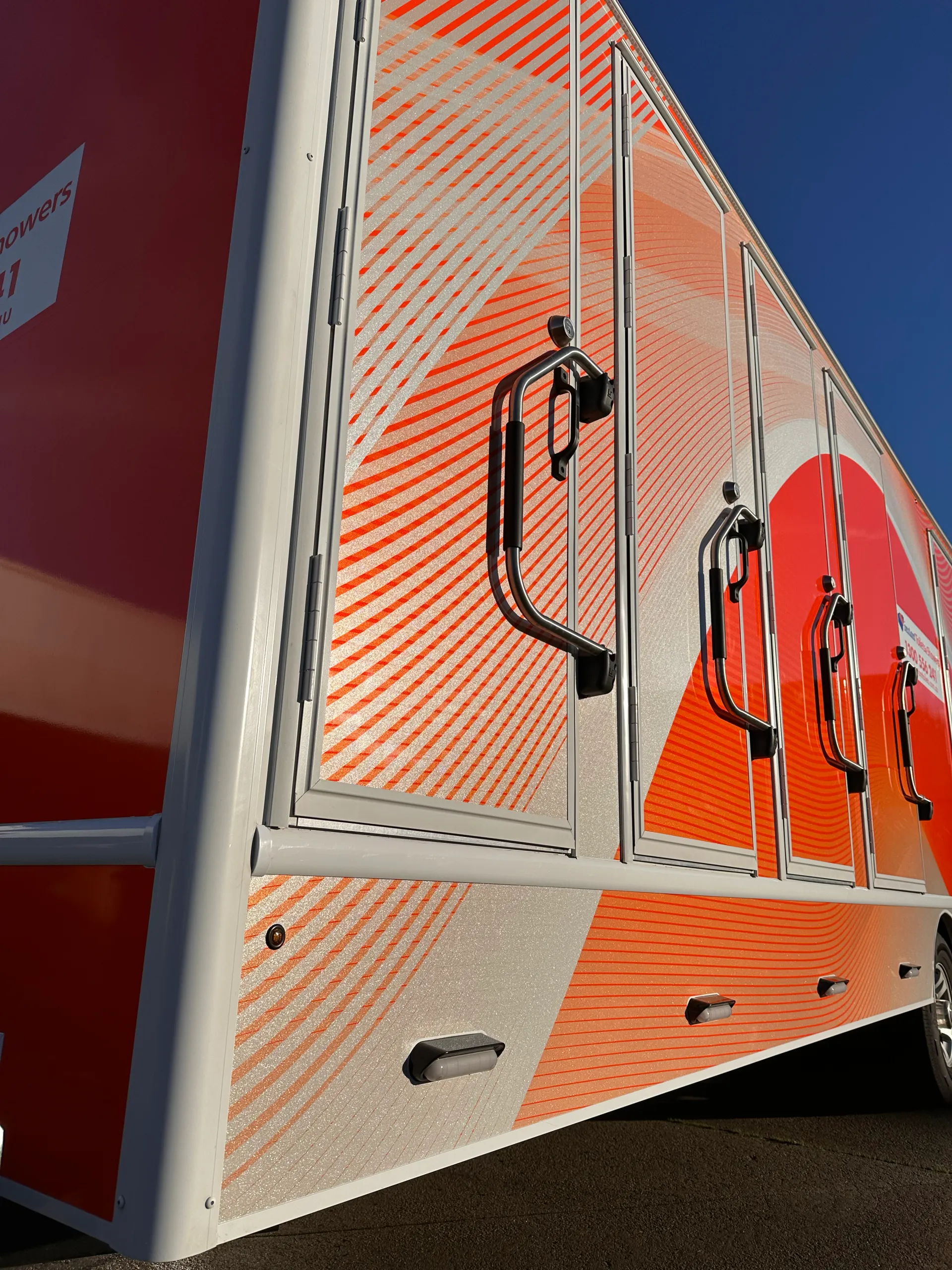 Low-angle detail of orange striped trailer graphics and black grab handles in sunlight