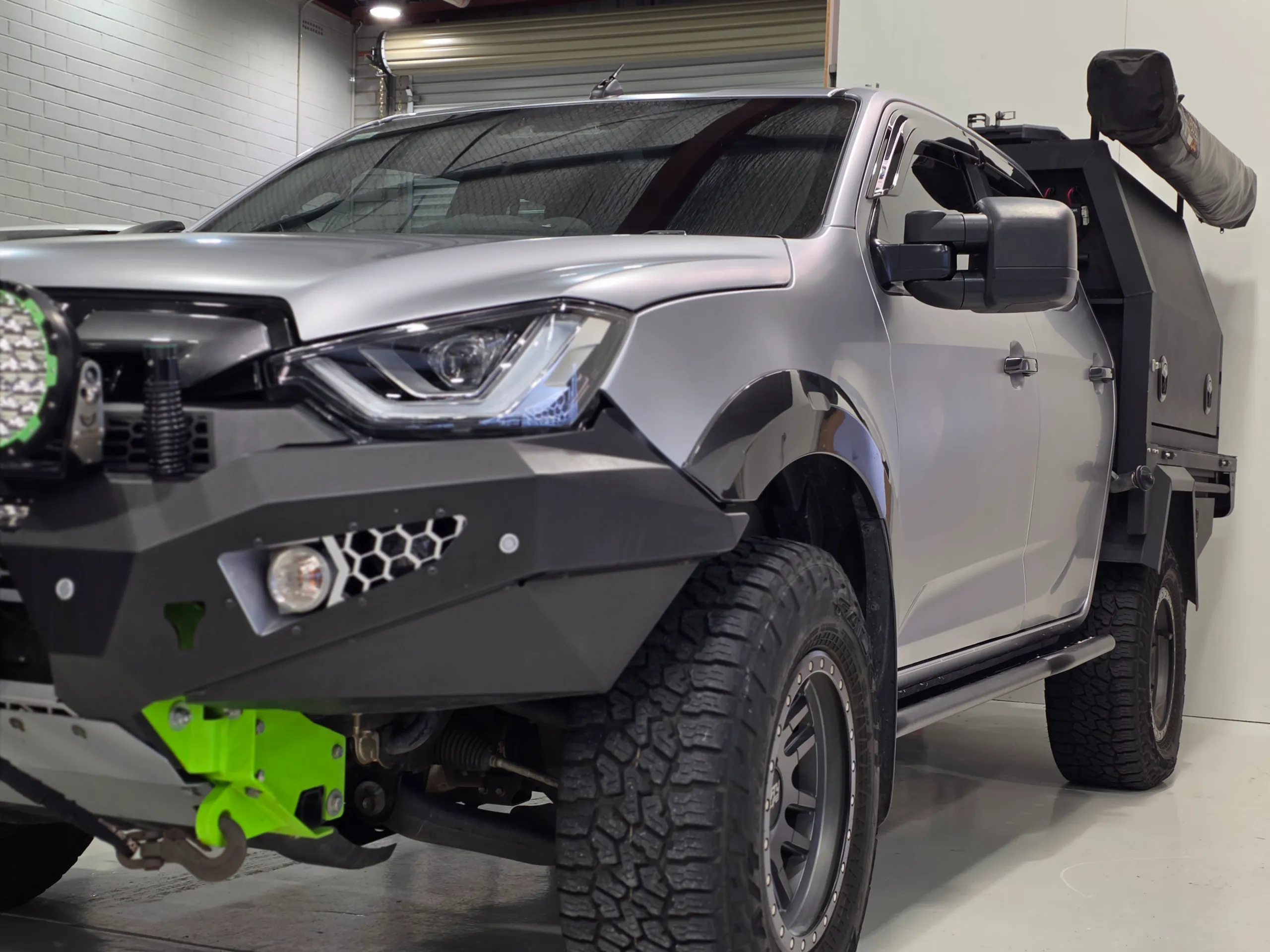 Silver Isuzu D-MAX with a satin finish, black canopy and off-road tyres in the workshop
