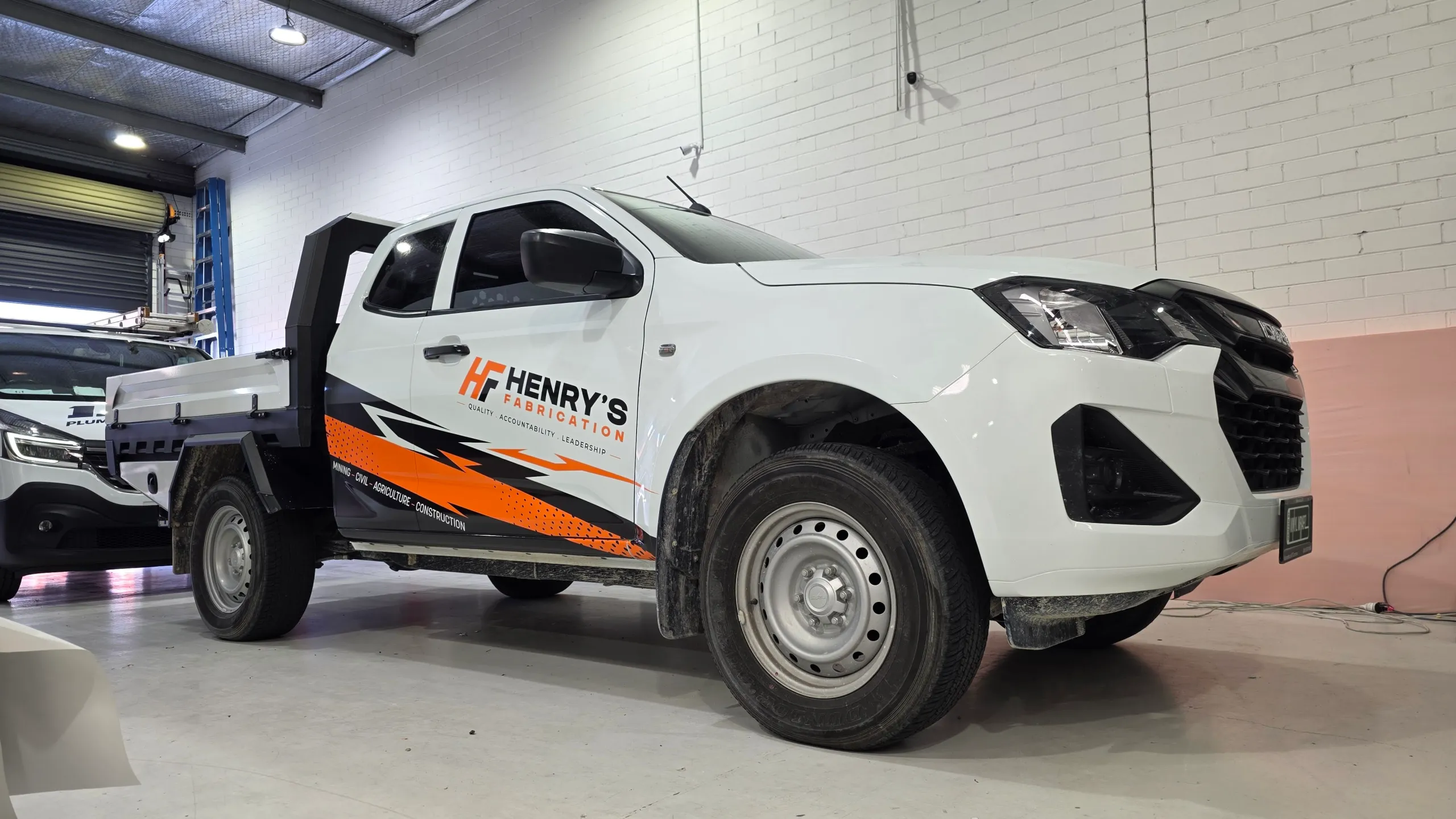 White Isuzu D-MAX tray ute with orange and black Henry’s Fabrication graphics