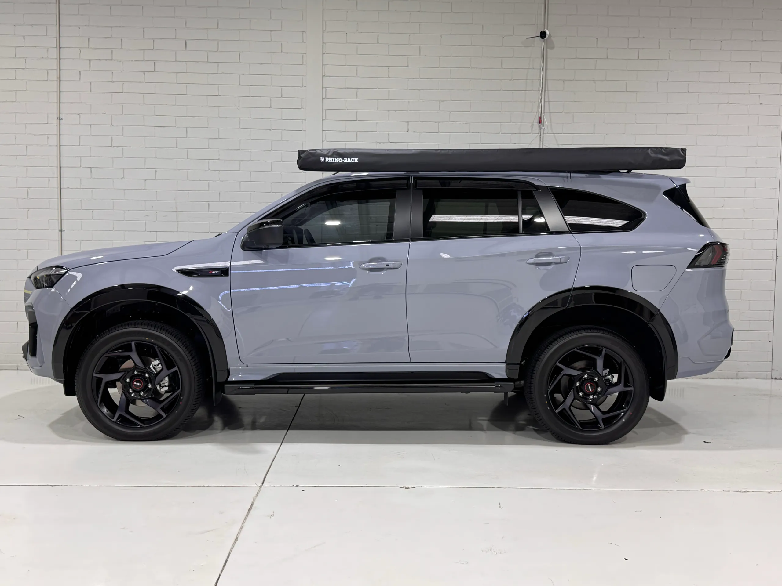 Side view of a gloss grey Isuzu MU-X with black wheels, roof rack and awning