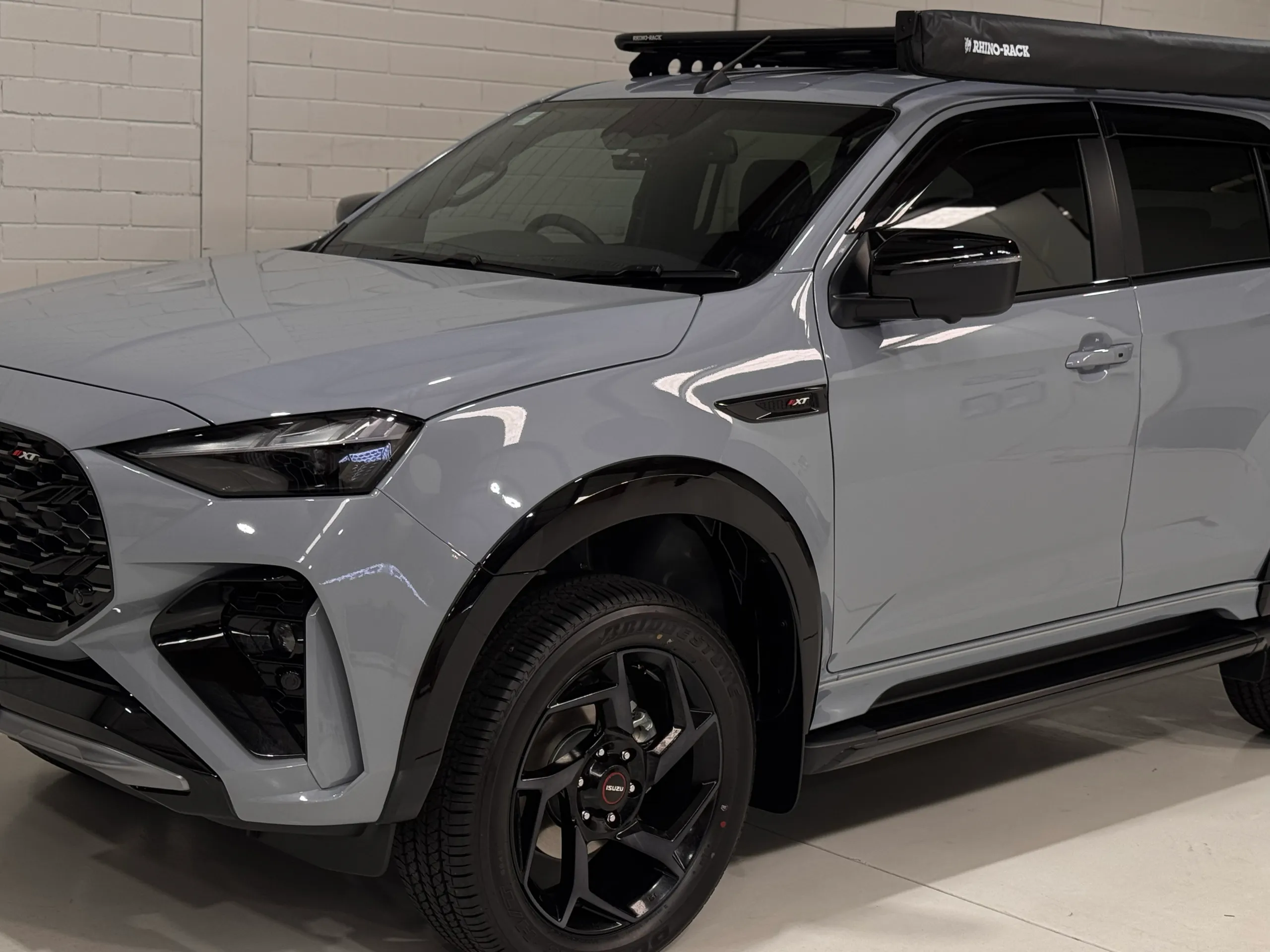 Front quarter and roof rack of a gloss grey Isuzu MU-X in the workshop