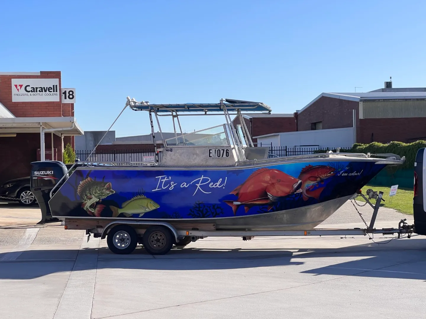 Blue boat wrap with colourful fish and It's a Red lettering viewed from the side outdoors