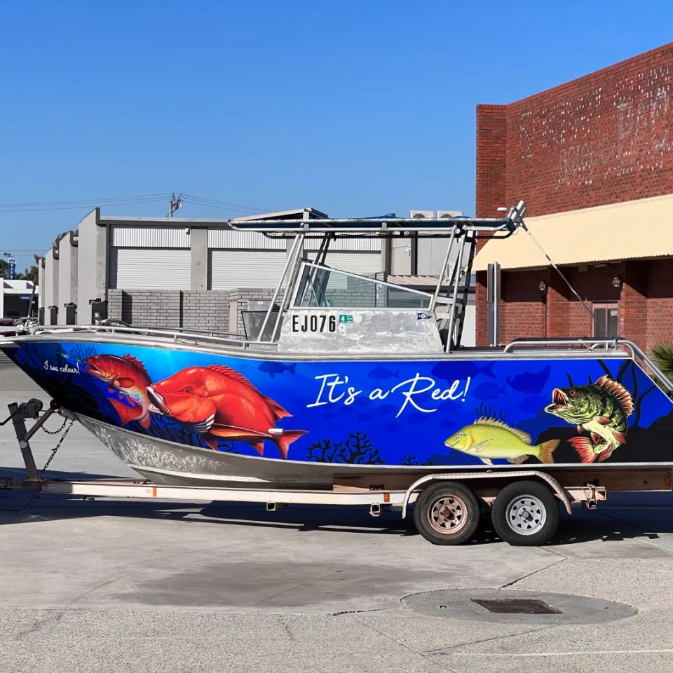 It's a Red boat with blue fish graphics along its hull on a trailer outdoors
