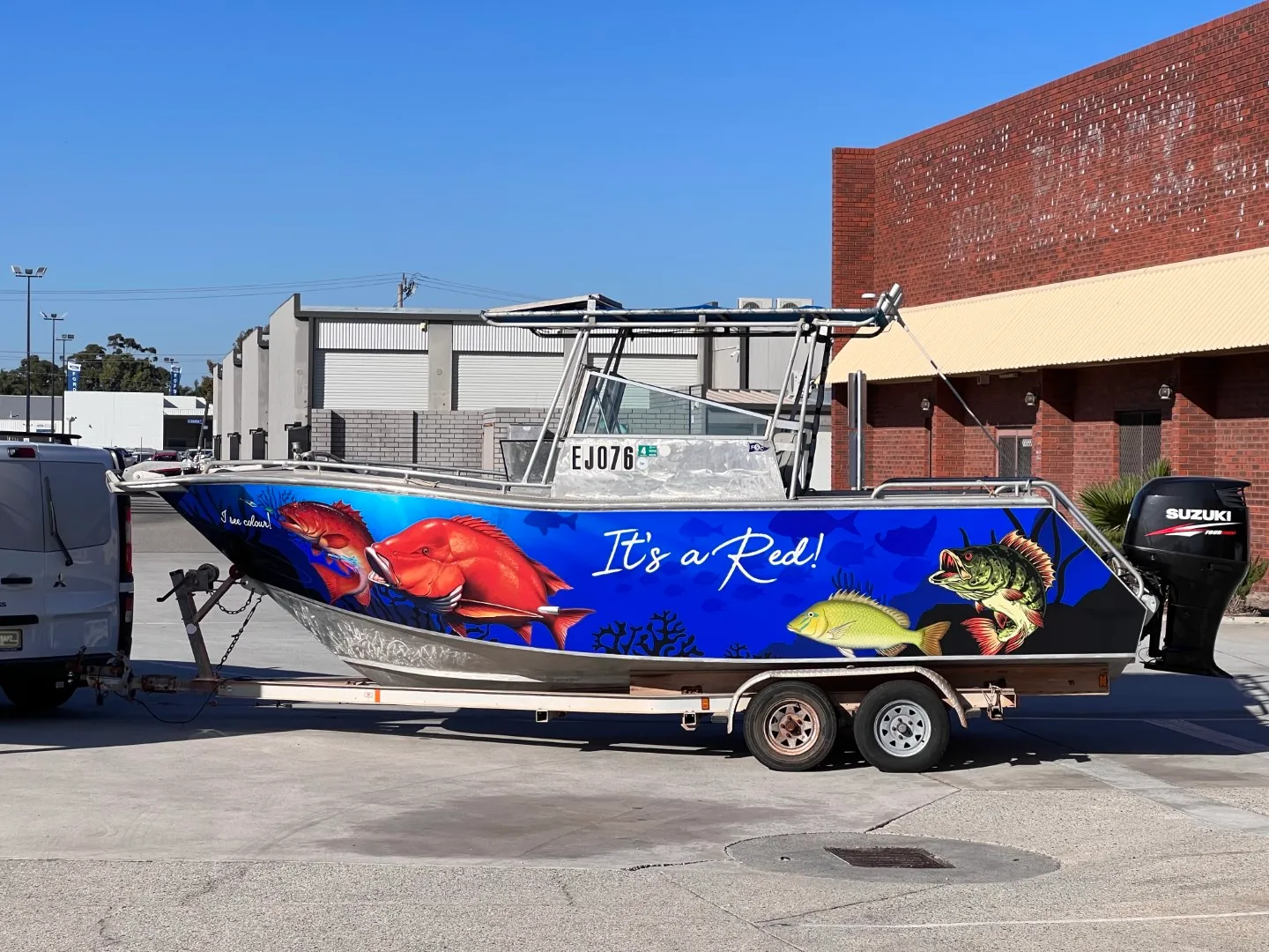 It's a Red boat with blue fish graphics along its hull on a trailer outdoors