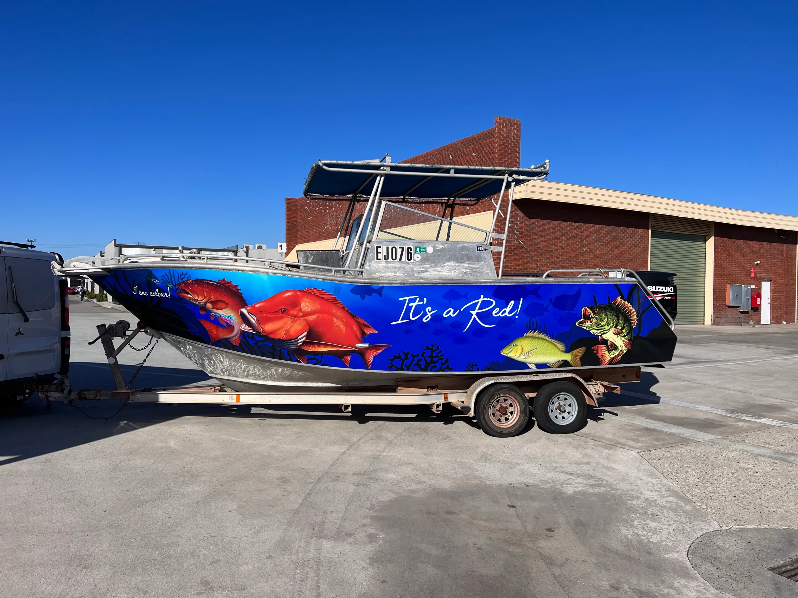 Side view of the boat's blue fish graphics and It's a Red lettering outside the workshop
