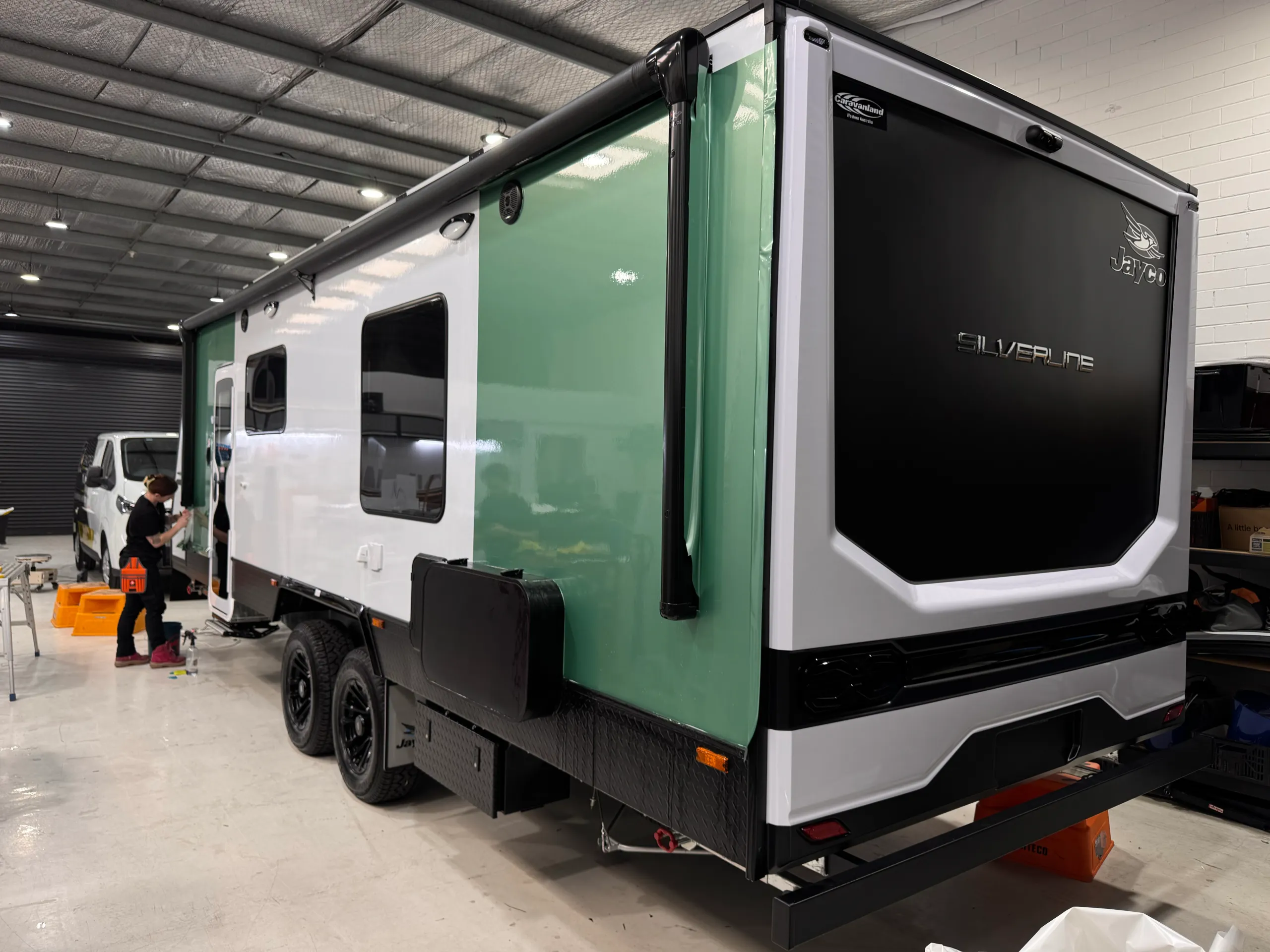 Green film being fitted along the Jayco Silverline caravan, with a white section still exposed